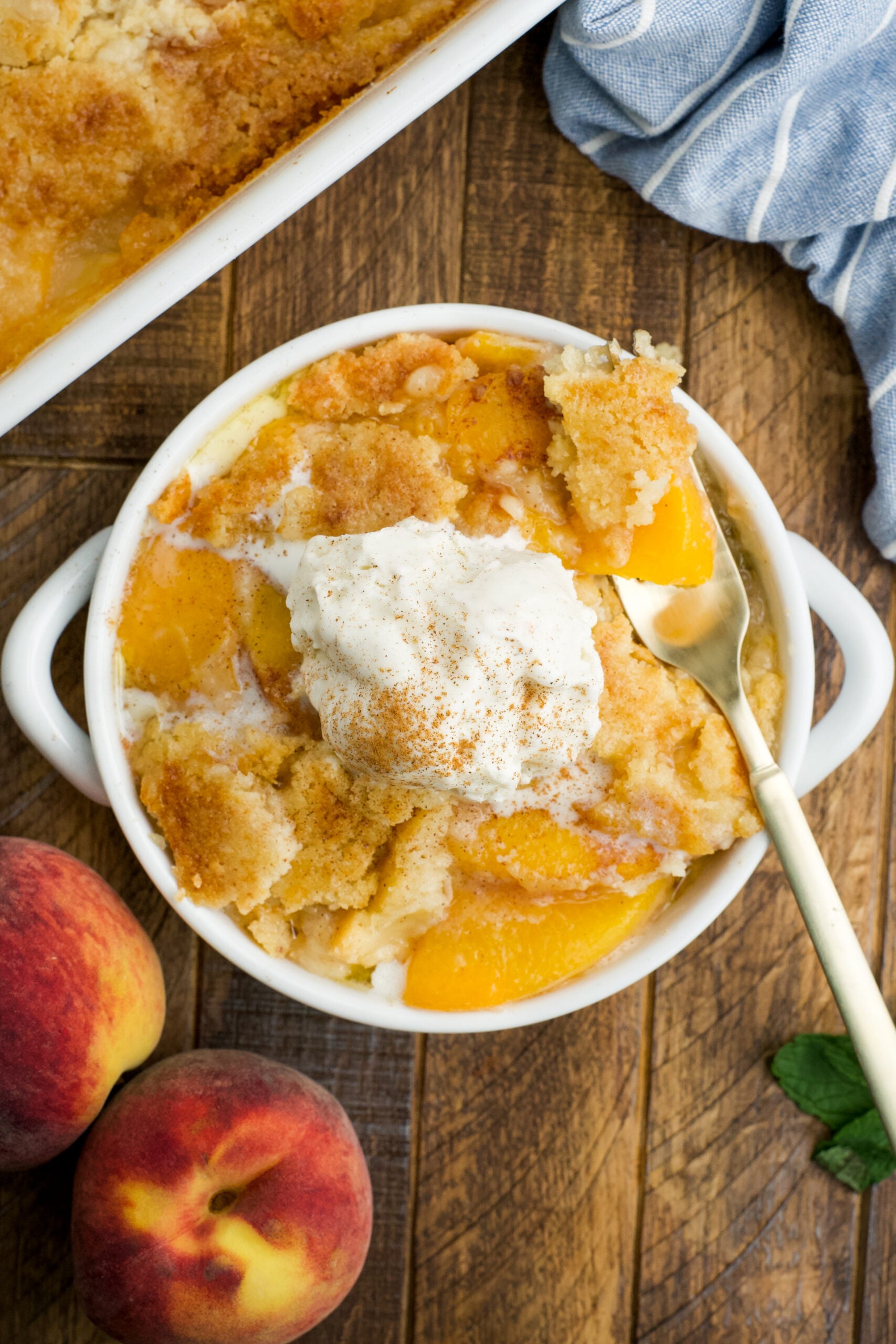 Overhead view of a serving of Peach Dump Cake in a white bowl topped with a scoop of vanilla ice cream.