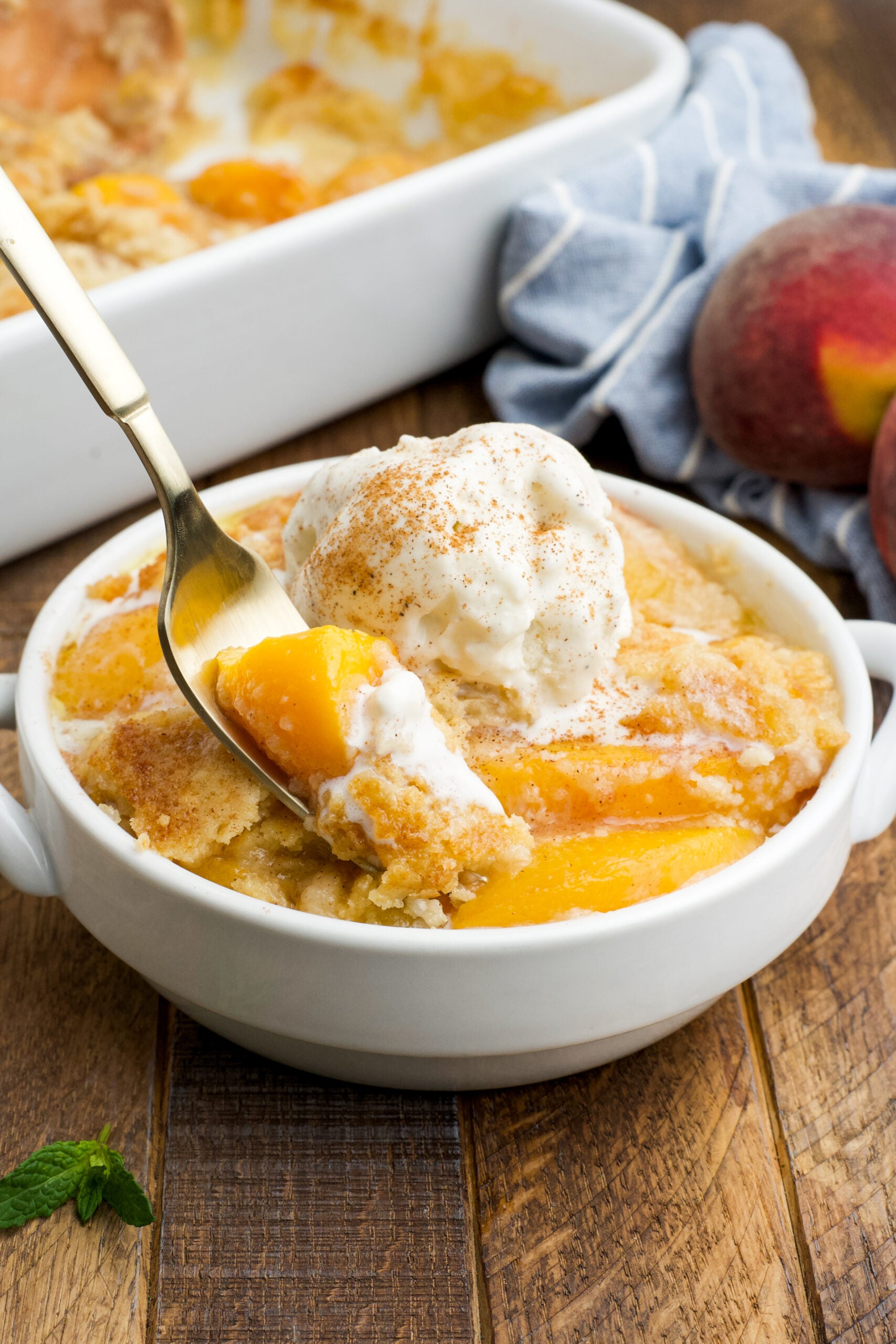 Front view of a serving of Peach Dump Cake in a white bowl with a gold fork removing a bite.