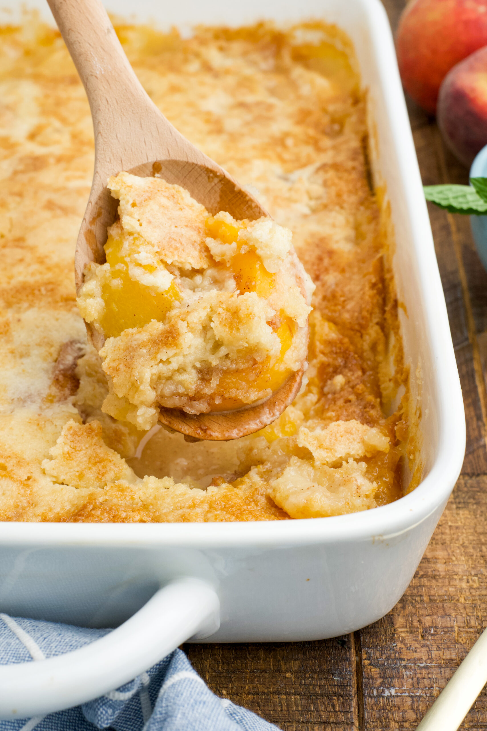 Close up view of a wooden spoon with a spoonful of Peach Dump Cake.