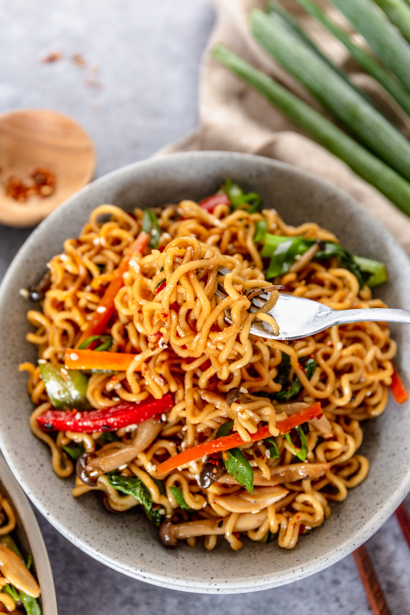 A fork removing Ramen Stir Fry from a speckled white bowl.