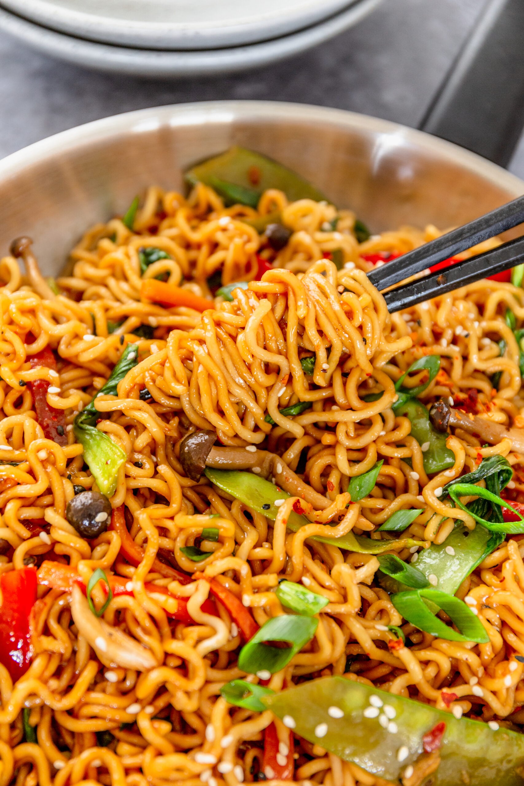 A pair of chop sticks lifting up a bite of the Ramen Stir Fry from a silver frying pan.