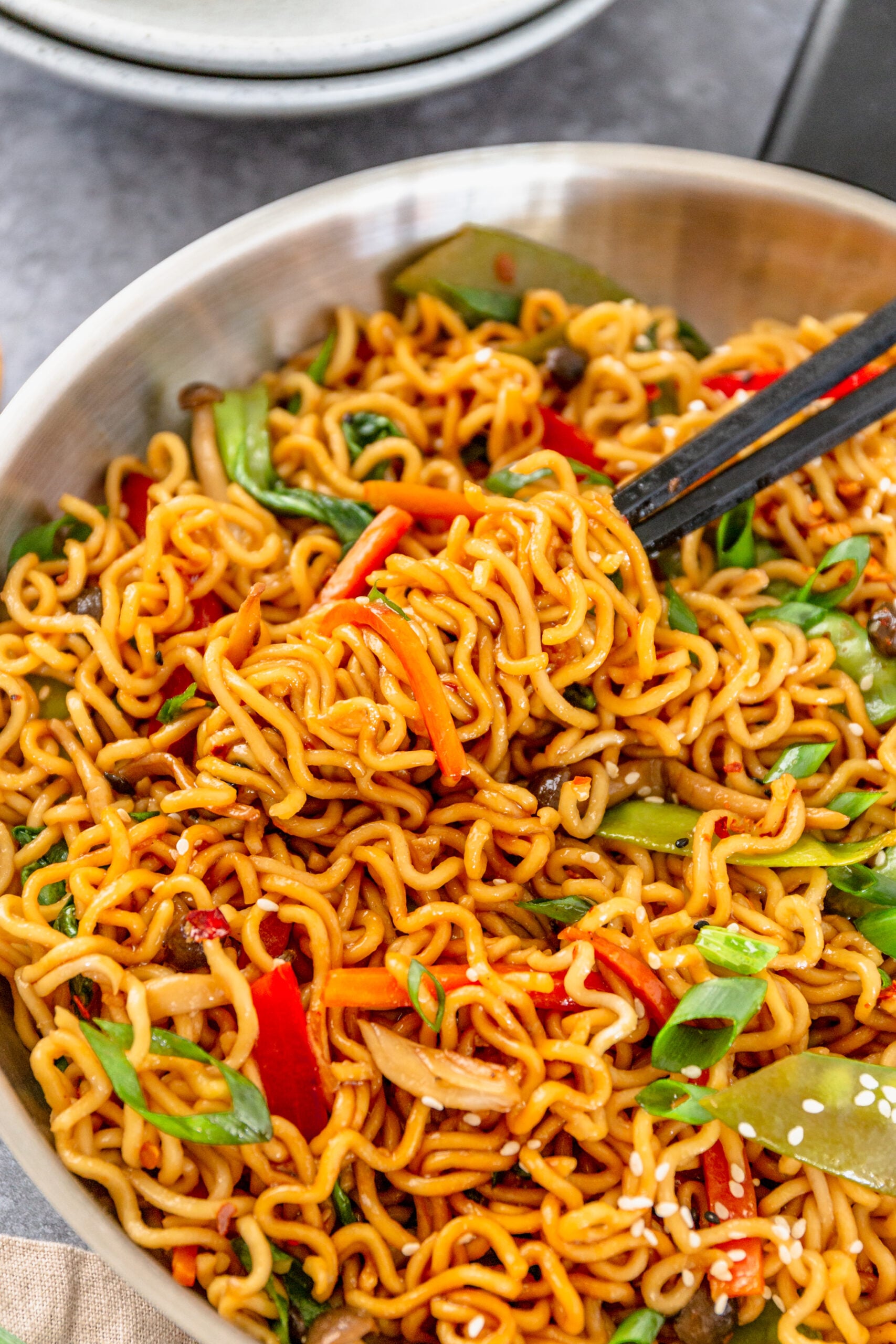 A pair of chop sticks removing Ramen Stir Fry from a silver frying pan.