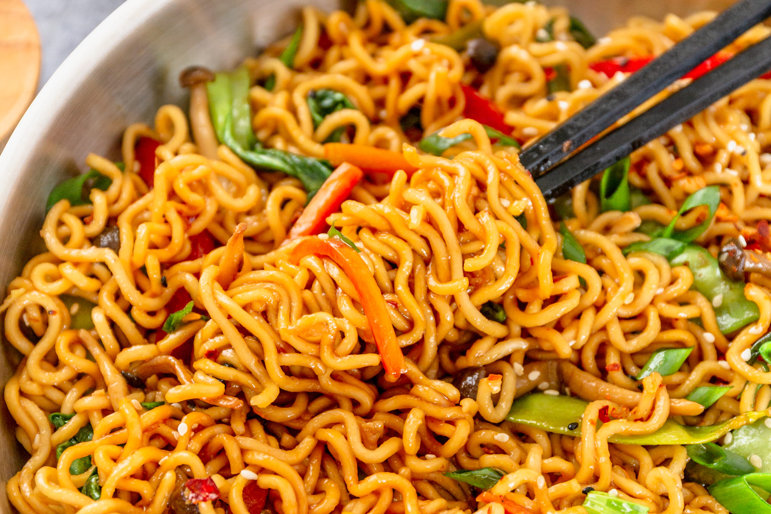 A pair of chop sticks removing Ramen Stir Fry from a silver frying pan.