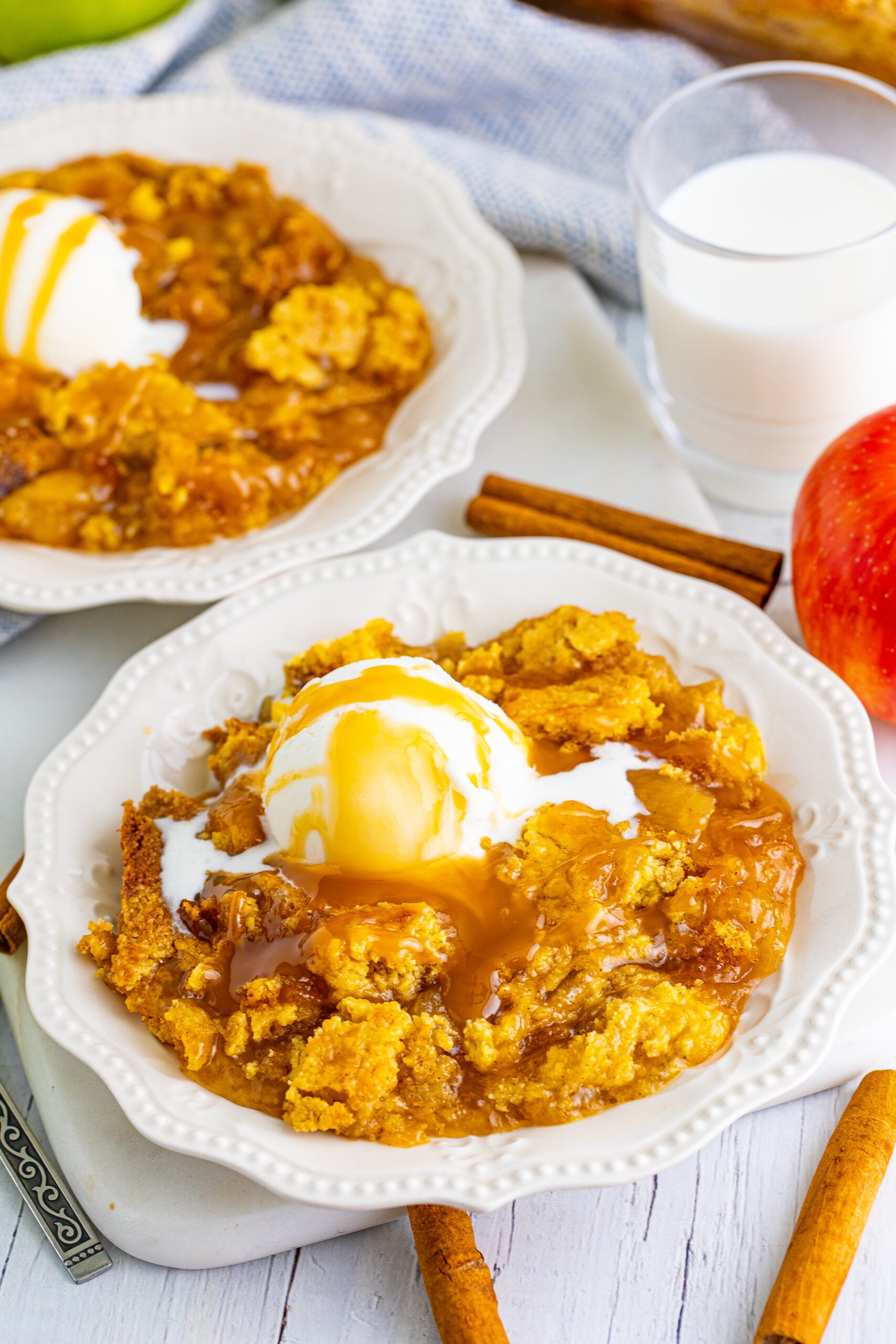 Close up shot of caramel apple dump cake topped with vanilla ice cream and caramel sauce.