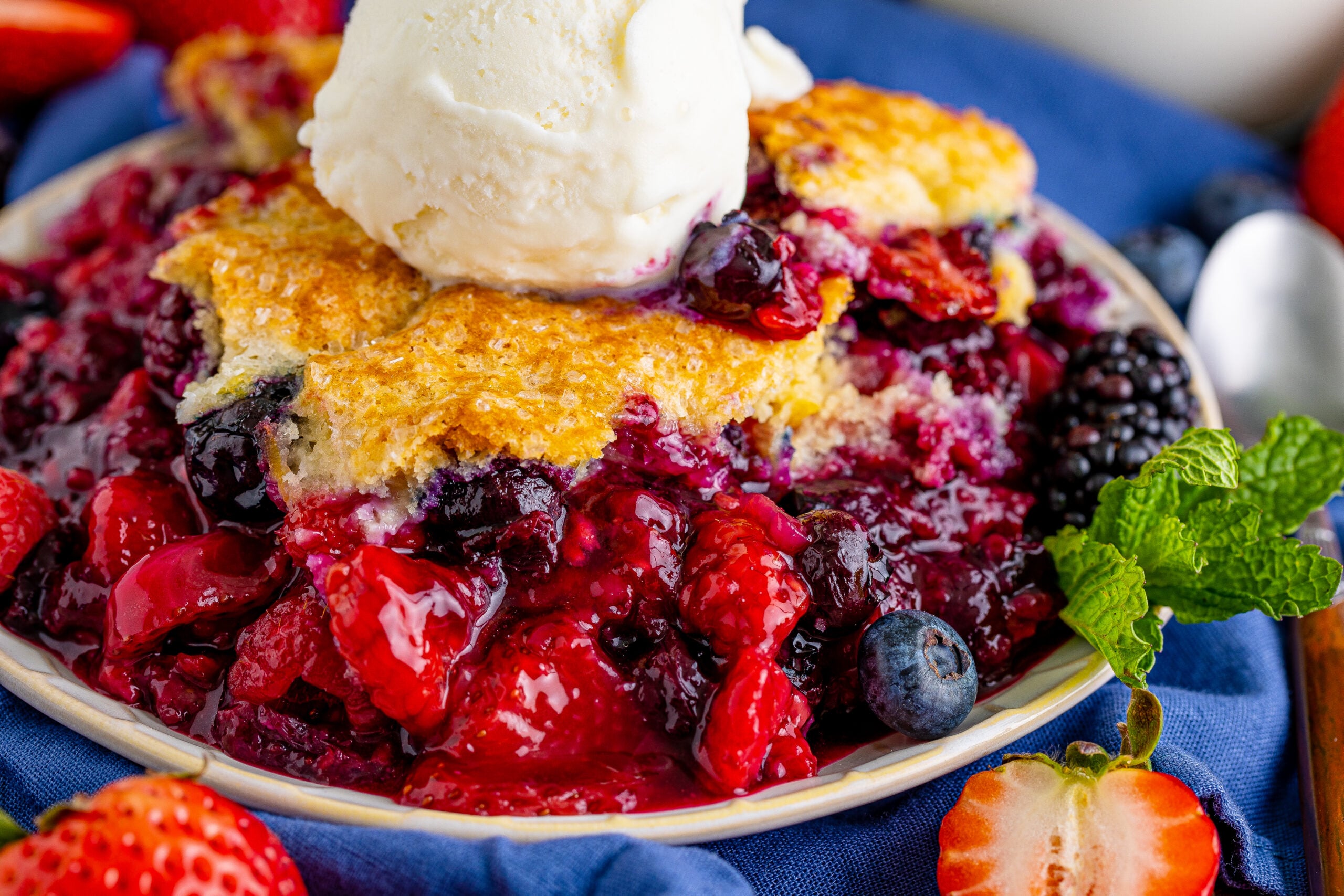 up close view of Mixed Berry Cobbler on a white dish served with a scoop of vanilla ice cream.