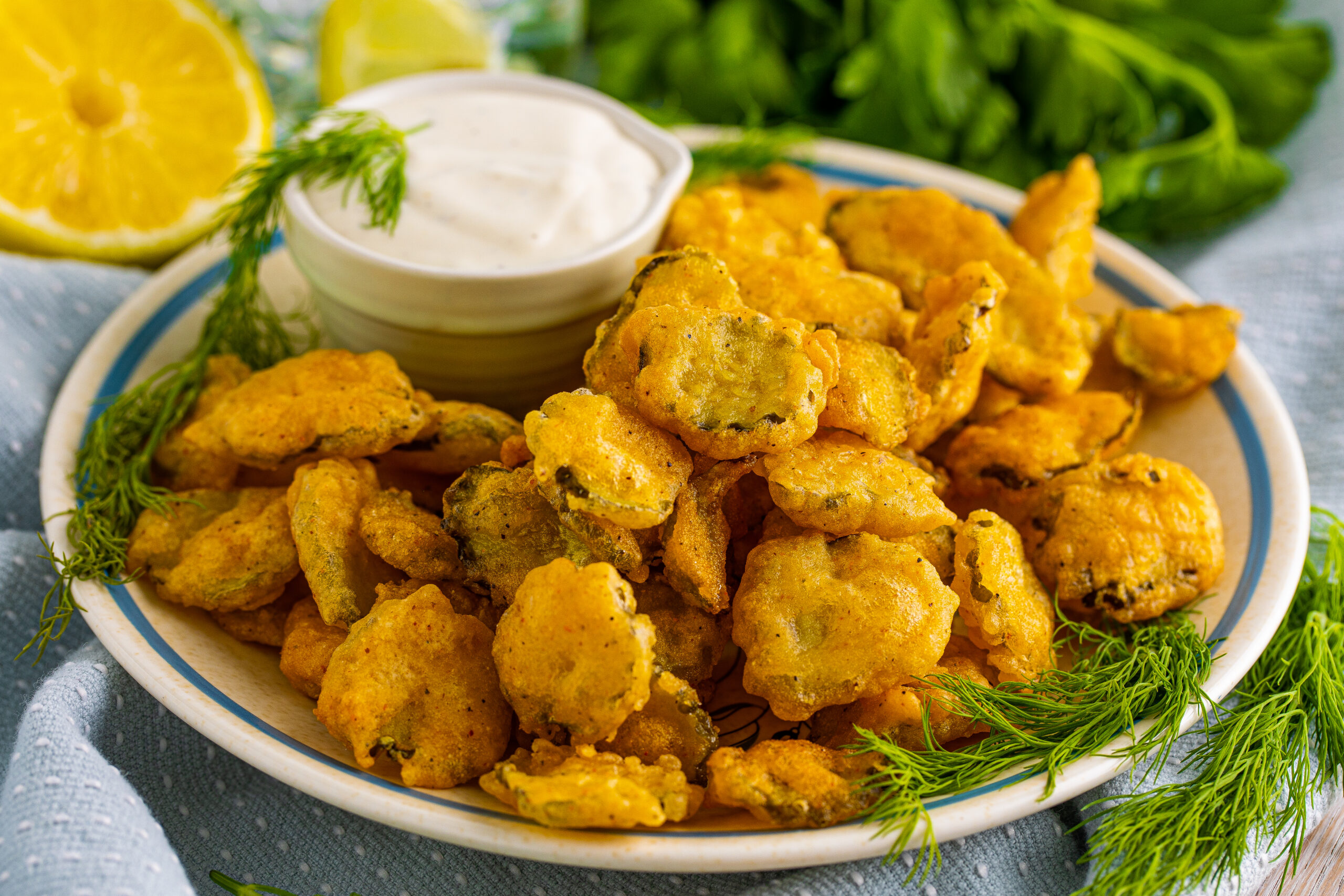 Close up shot of Fried Pickles on a white plate with ranch and fresh dill in the background.