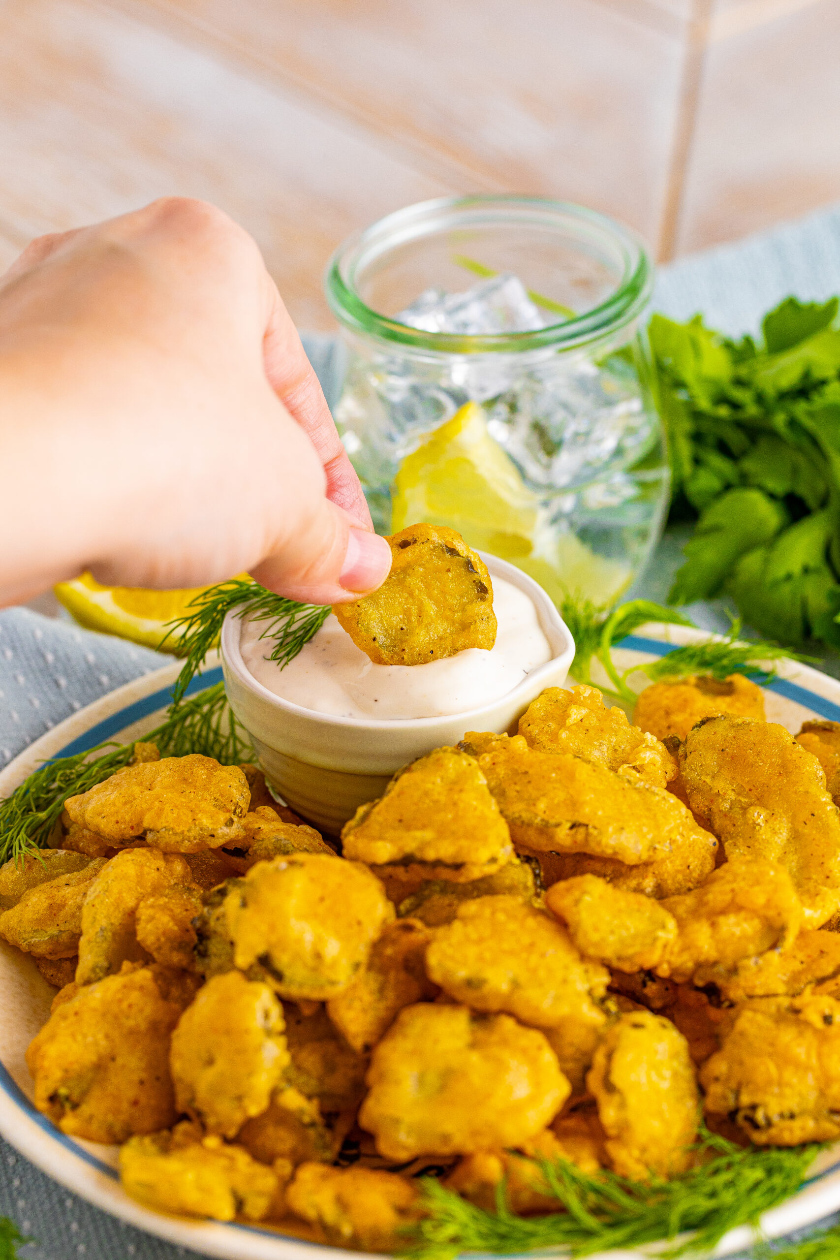 A hand dipping a fried pickle into ranch sauce.