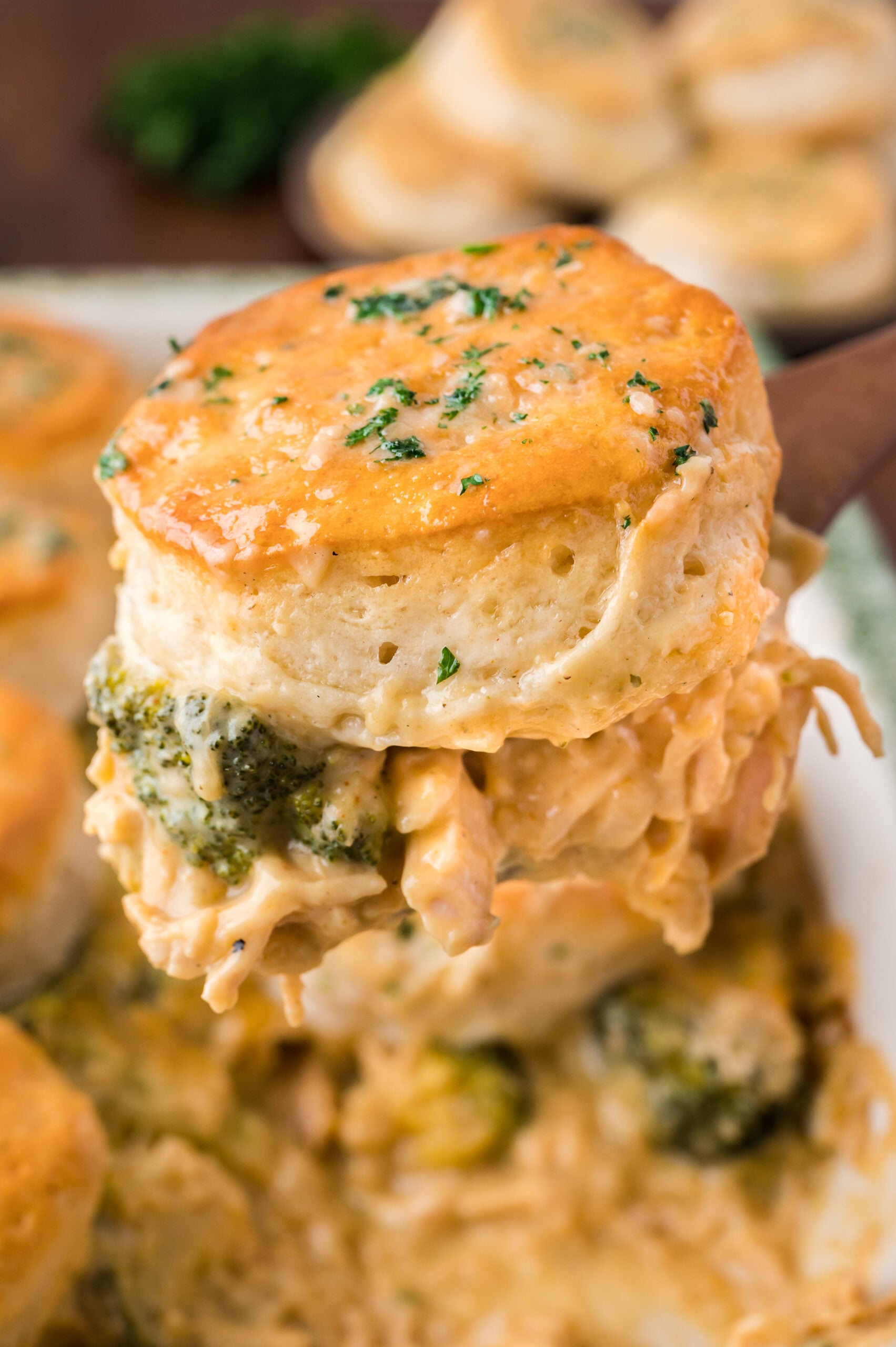 Close up view of a serving of Broccoli Cheddar Biscuit Casserole on a wooden spoon.