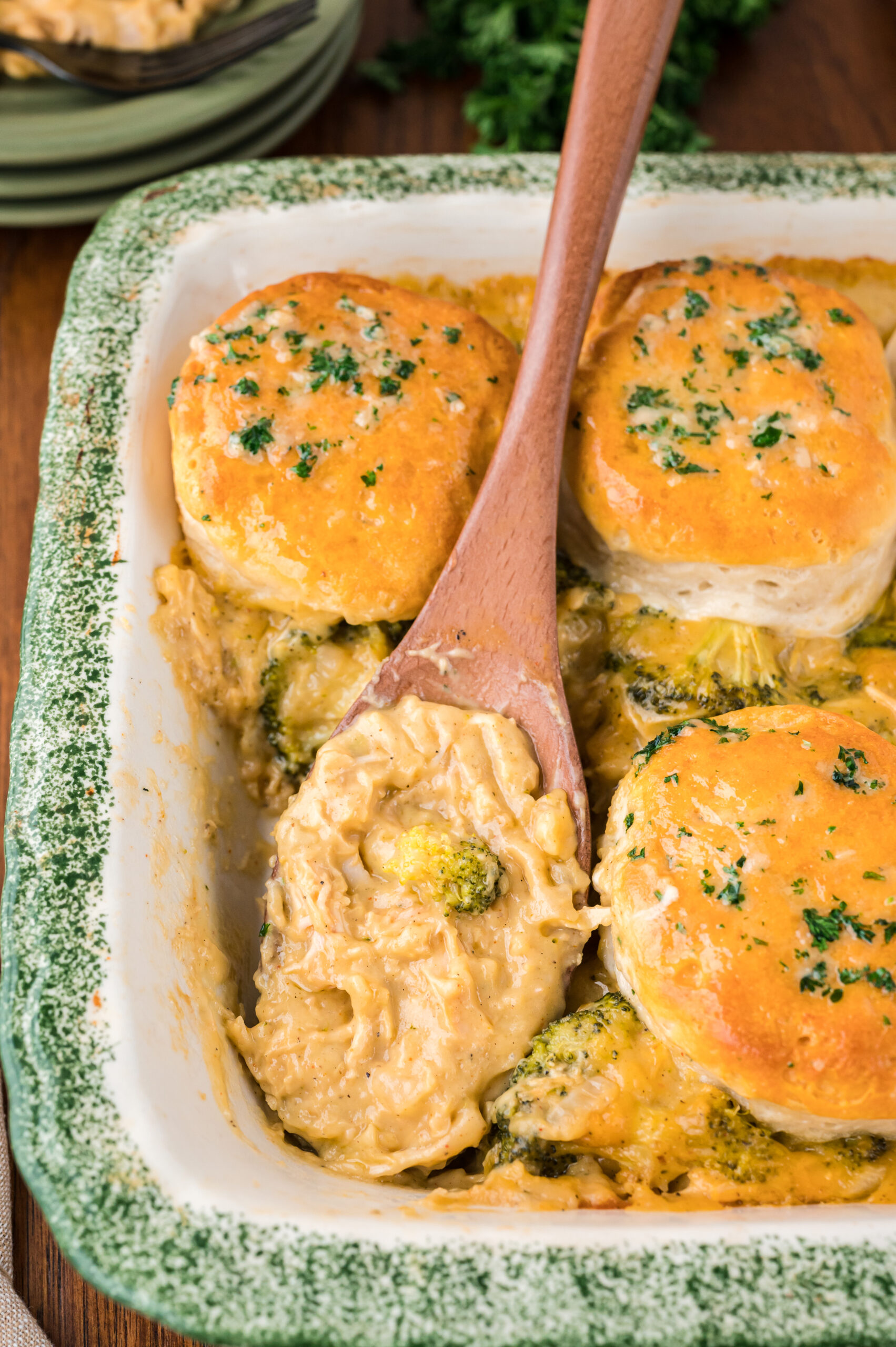 Close up view of a wooden spoon removing a serving of Broccoli Cheddar Biscuit Casserole.