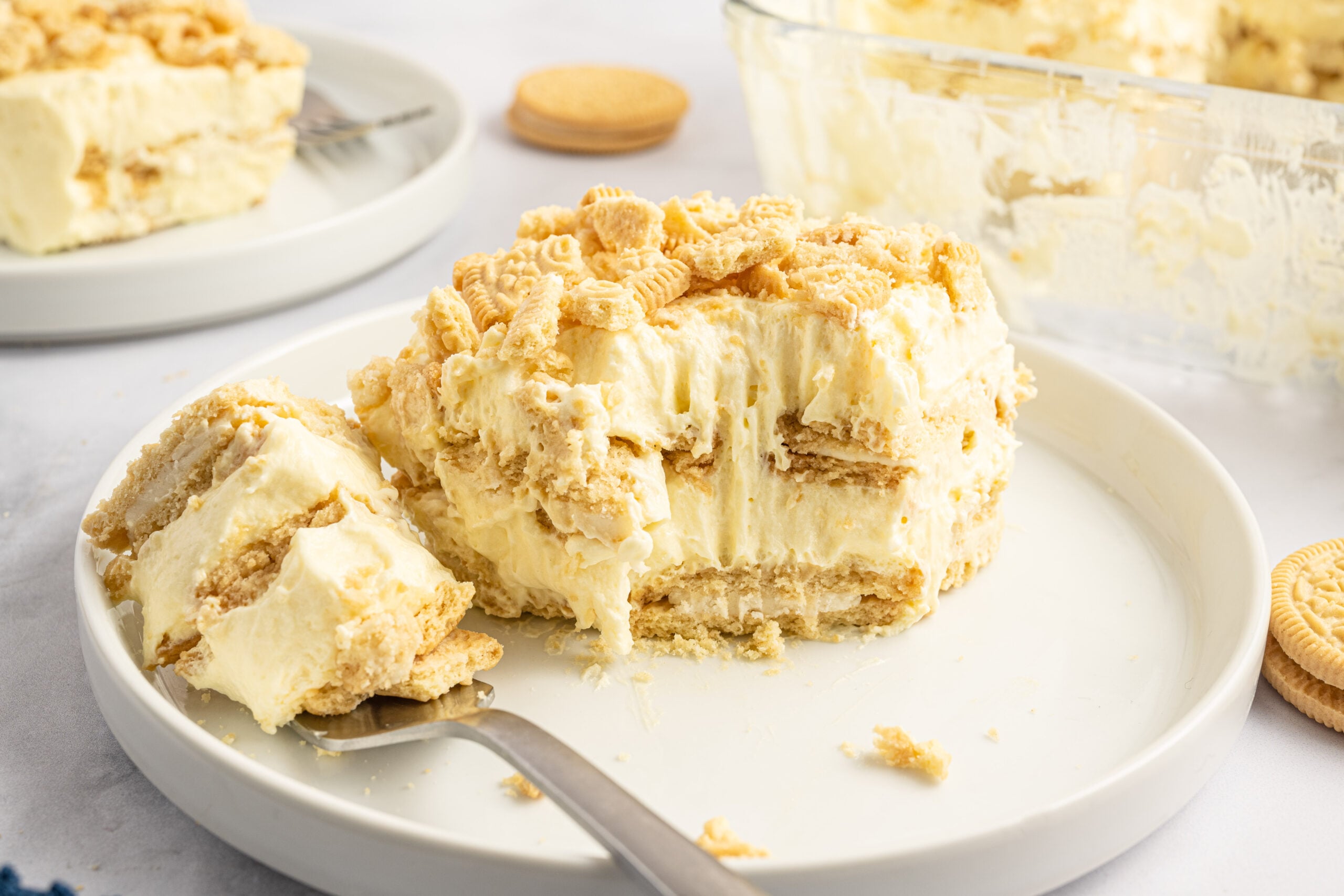Front view of a slice of Golden Oreo Icebox Cake on a white plate with a bite removed by a silver fork.