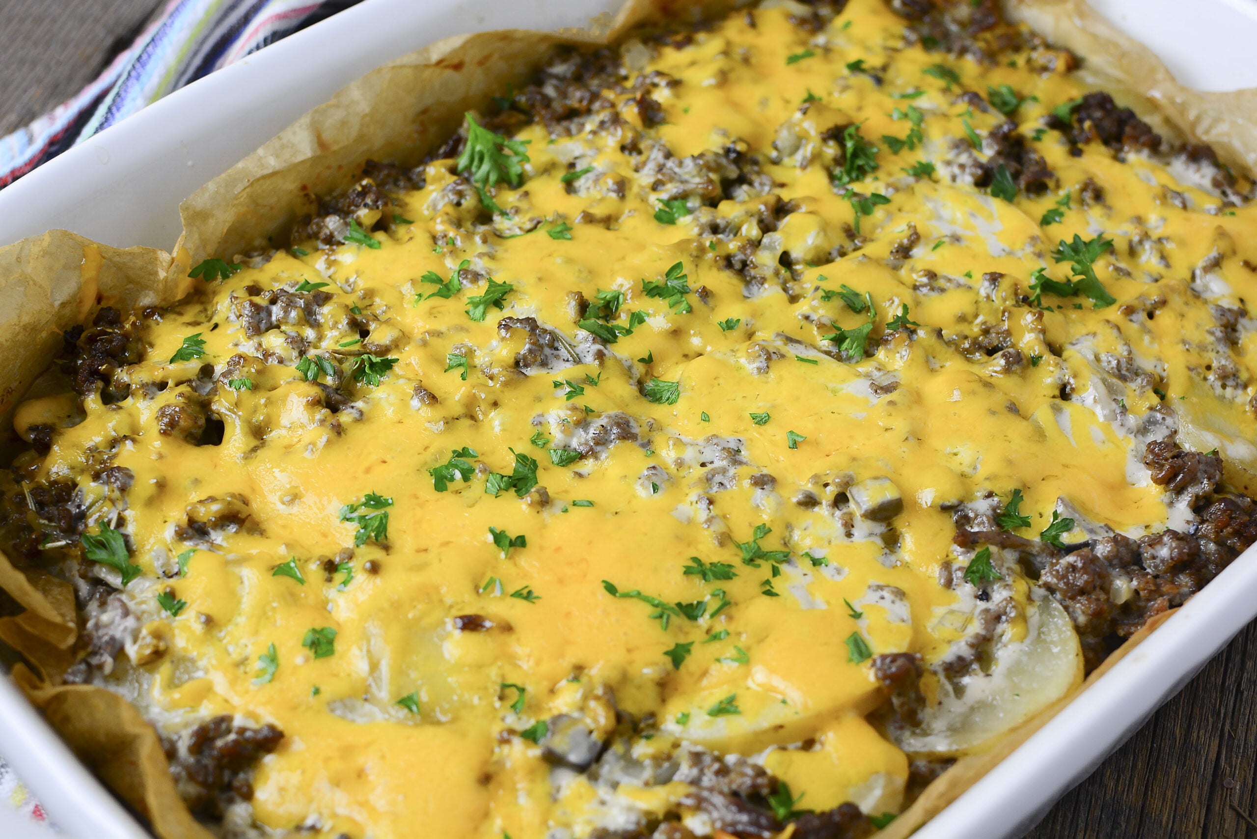 Ground Beef and Potato Casserole smothered in cheeses in a white dish topped with parsley. 
