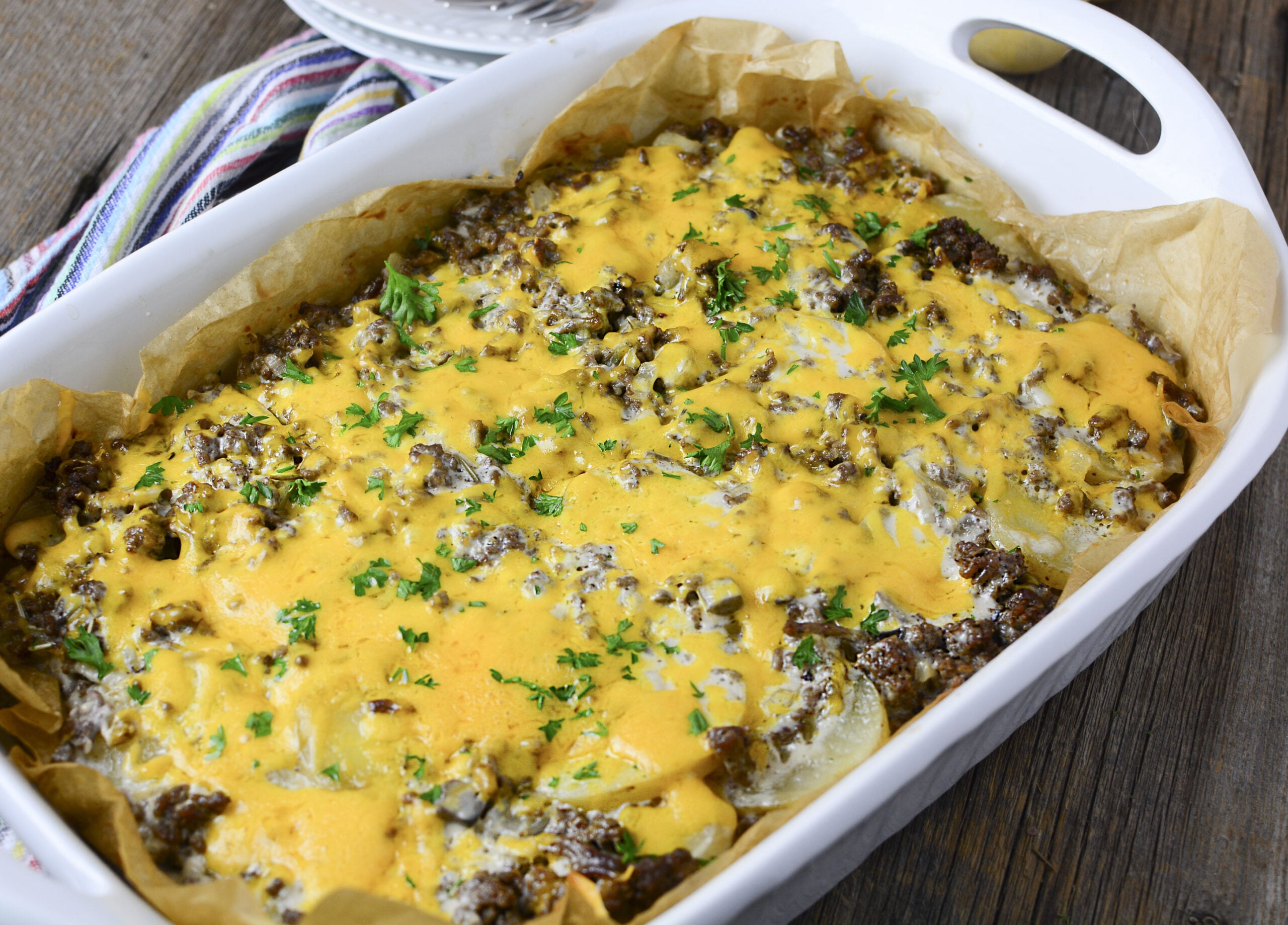 Side view of the Ground Beef and Potato Casserole smothered in cheeses in a white baking dish