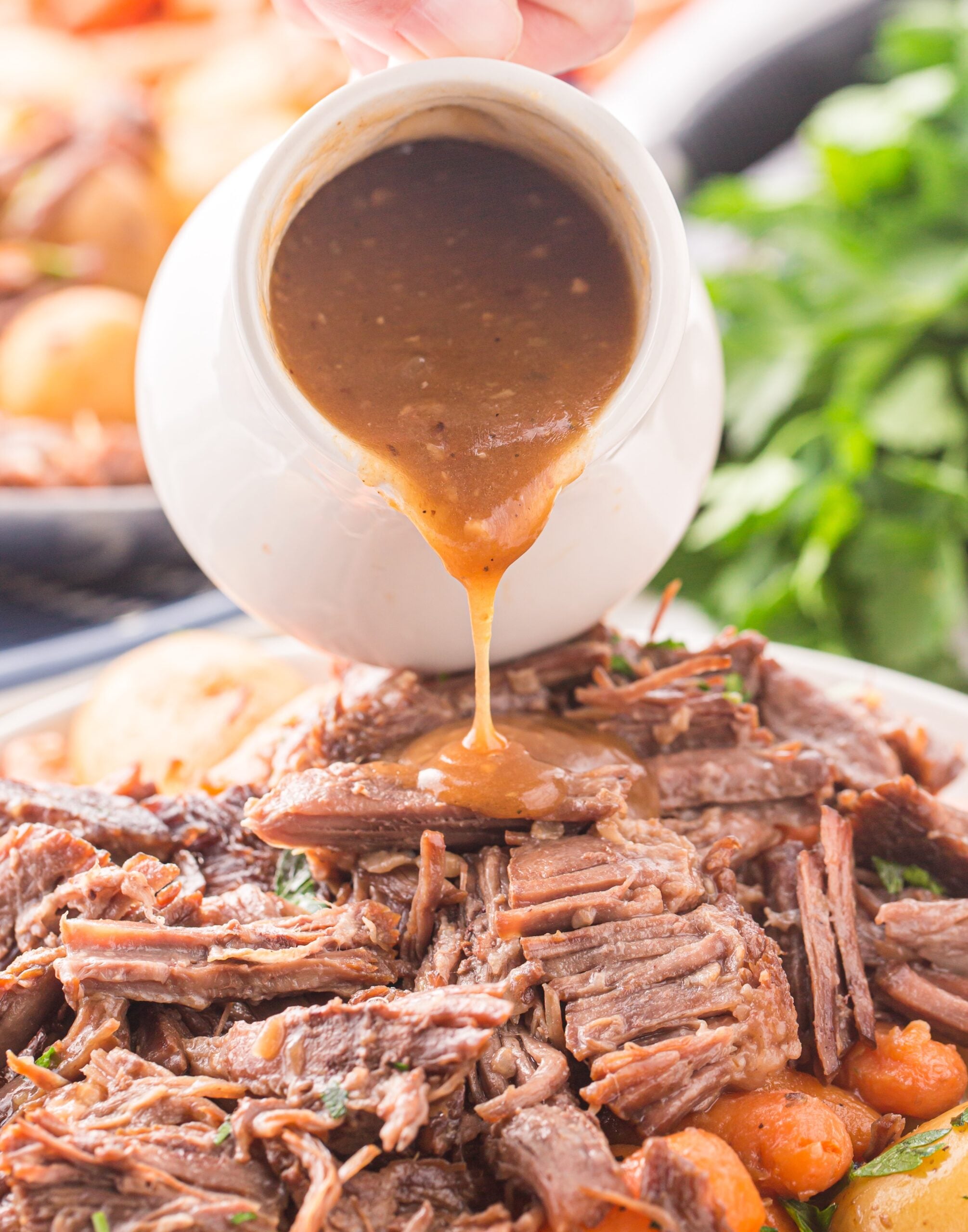 Pouring gravy from a white gravy boat onto the pot roast.