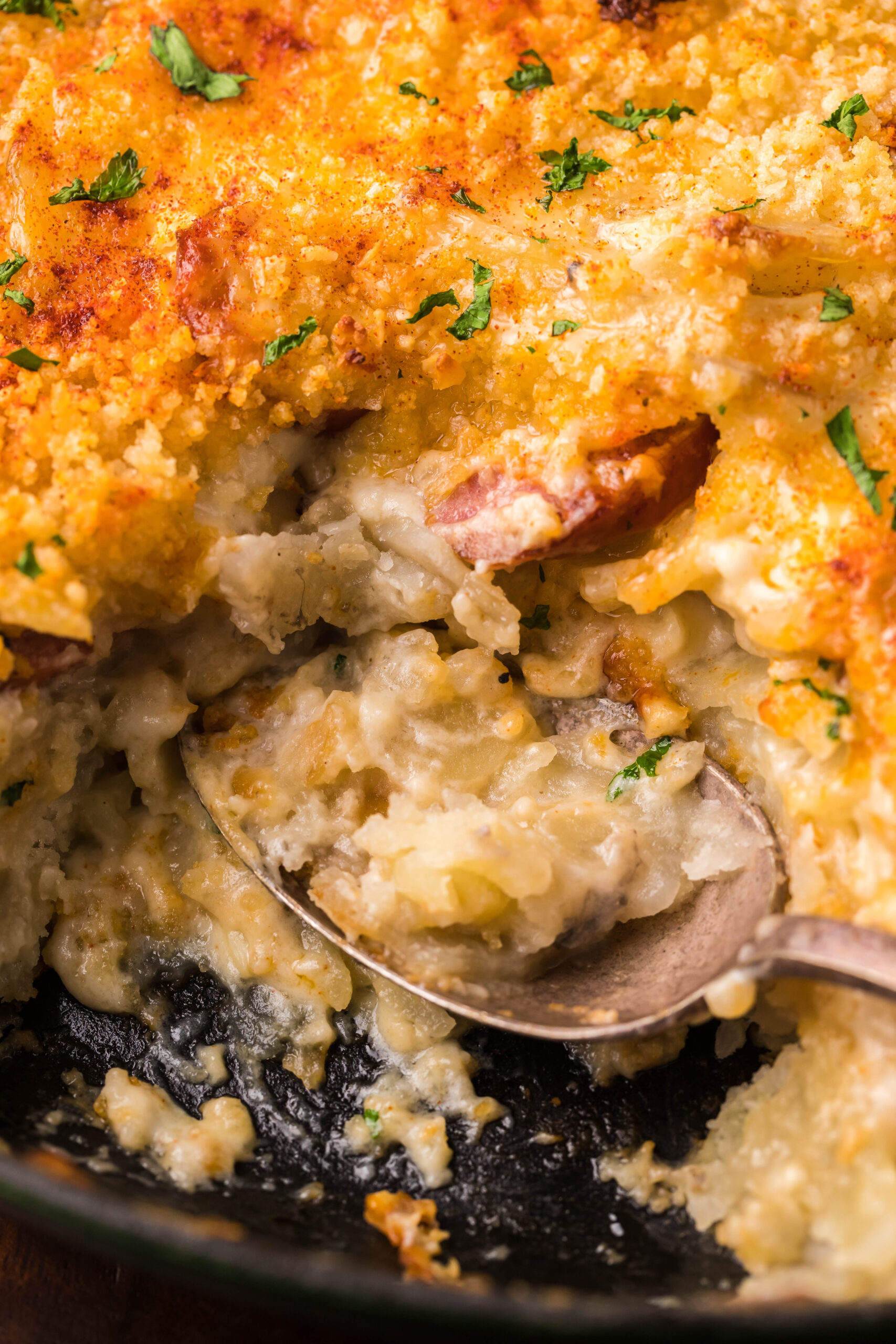 Au Gratin Potatoes & Sausage in a cast iron skillet with a spoon scooping some