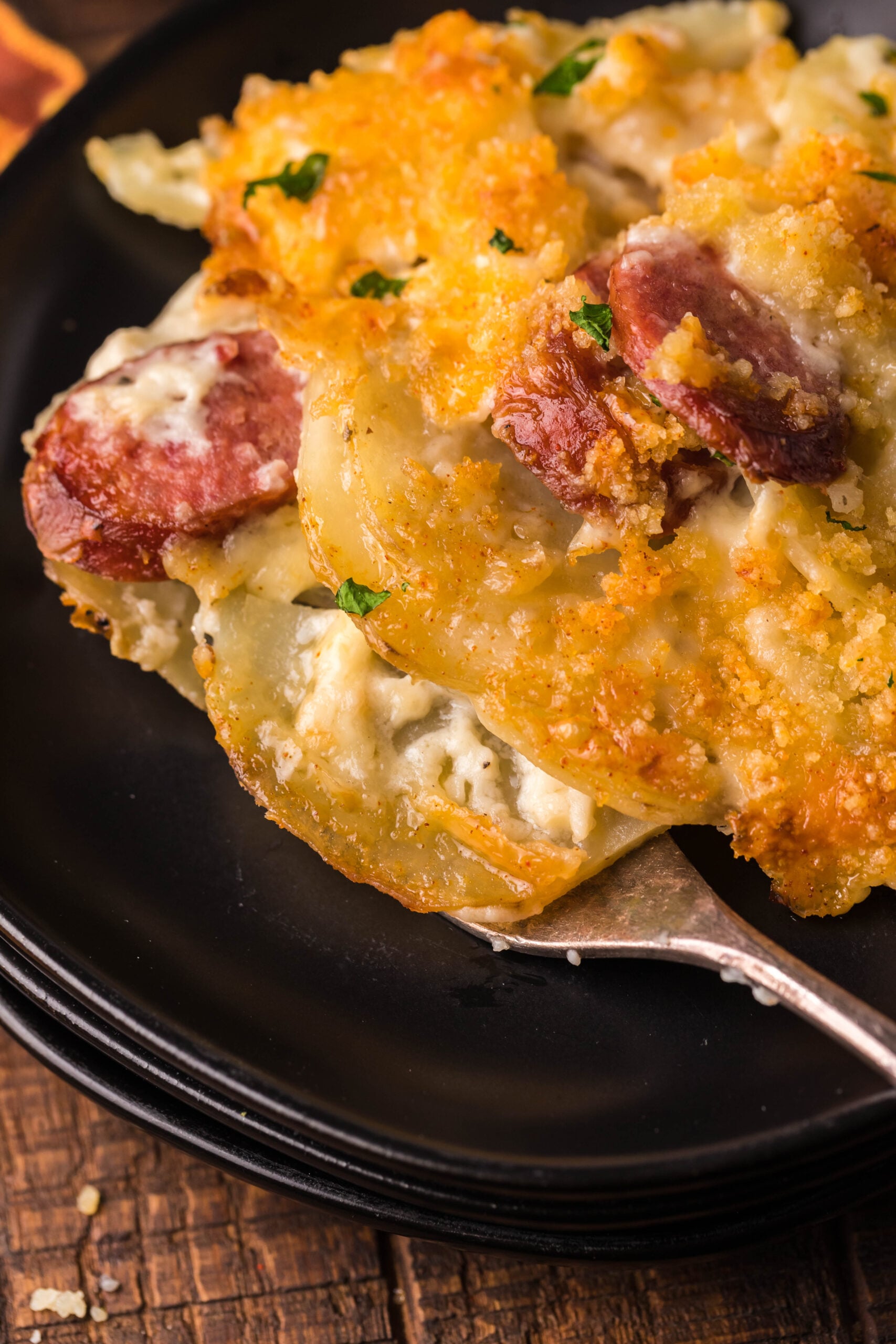 Close up view of a serving of Au Gratin Potatoes & Ham on a black plate served with a silver fork.