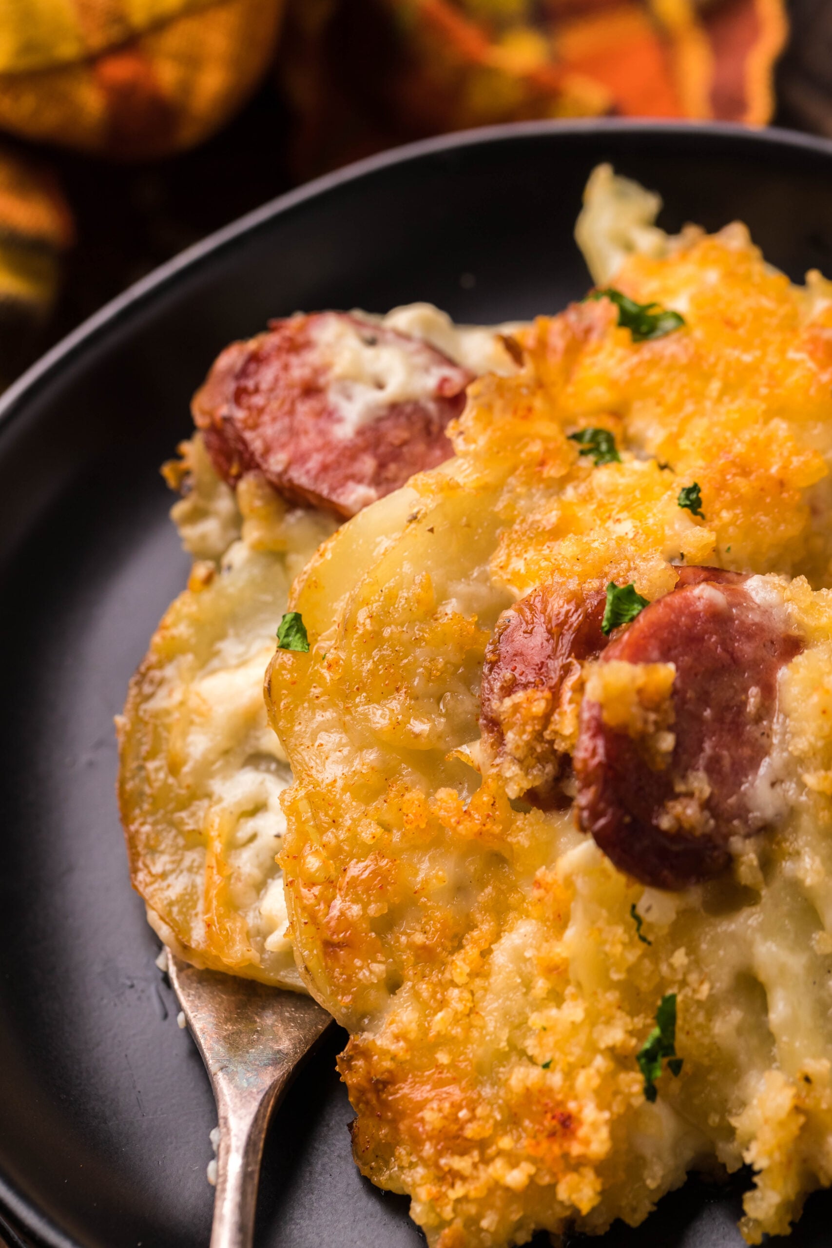 Close up view of a serving of Au Gratin Potatoes & Ham on a black plate served with a silver fork.