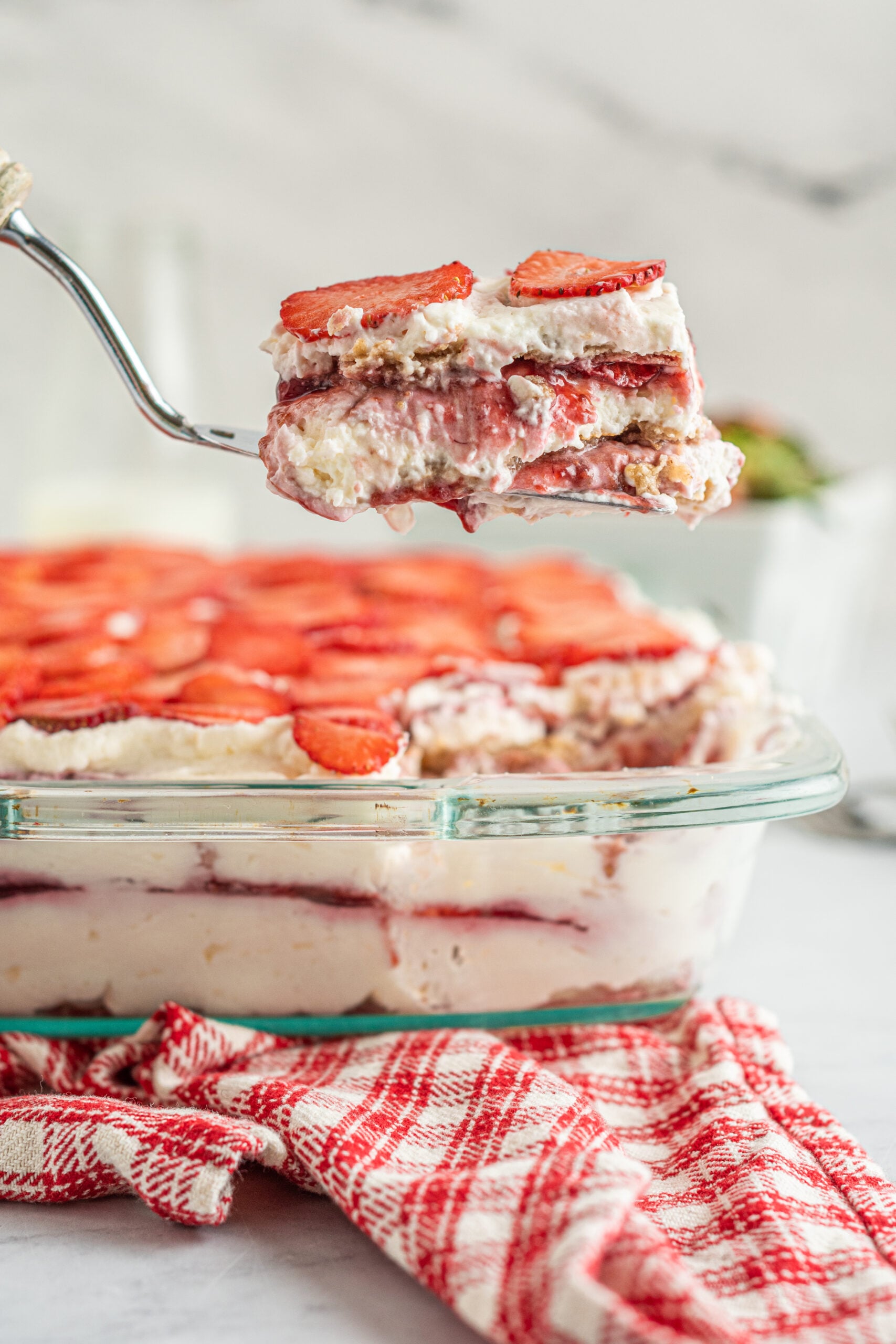 Strawberry Icebox Cake in a baking dish with a piece being removed with a silver spatula.