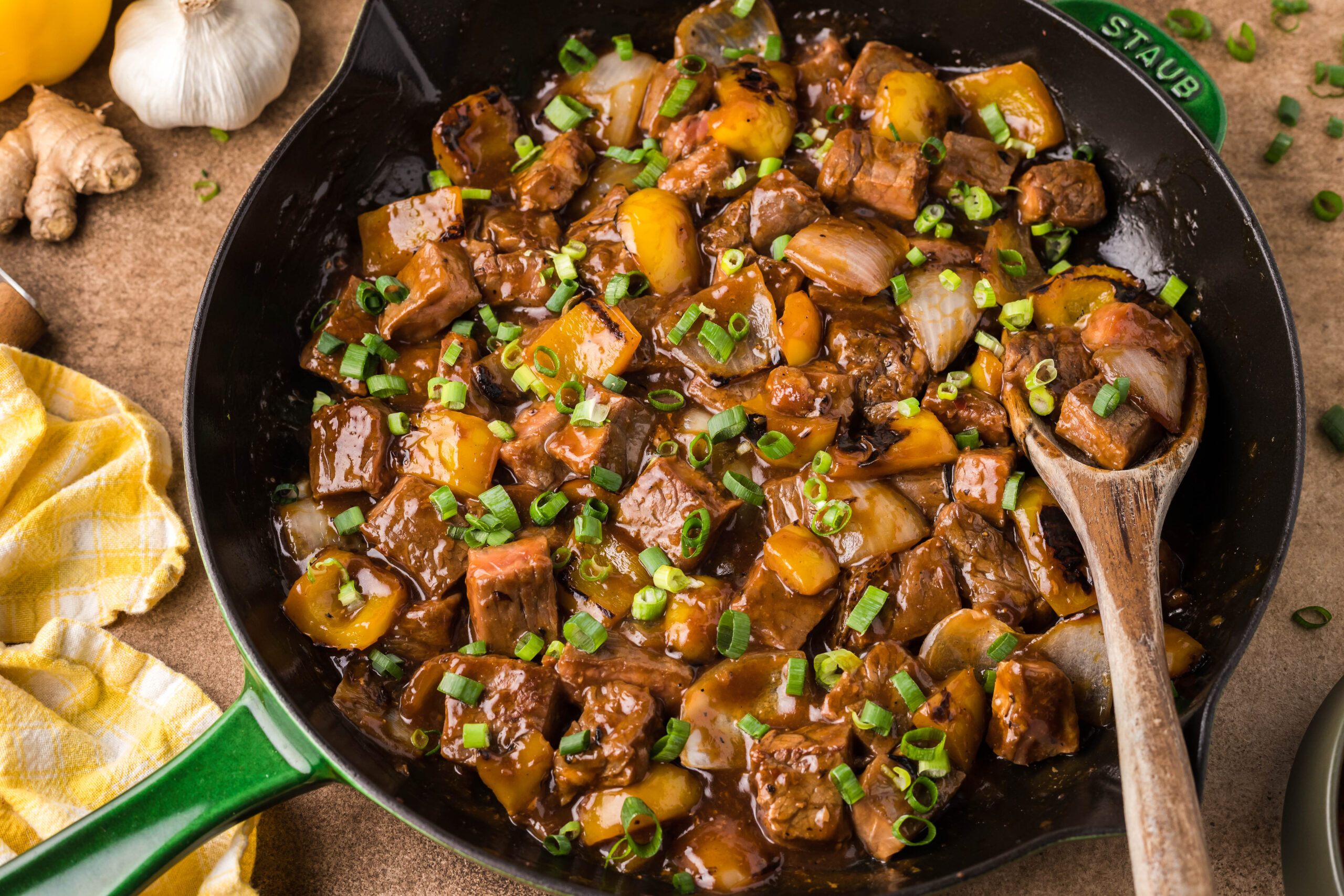 Front view of Teriyaki Steak Bites in a black and green skillet with a wooden spoon in the pan,