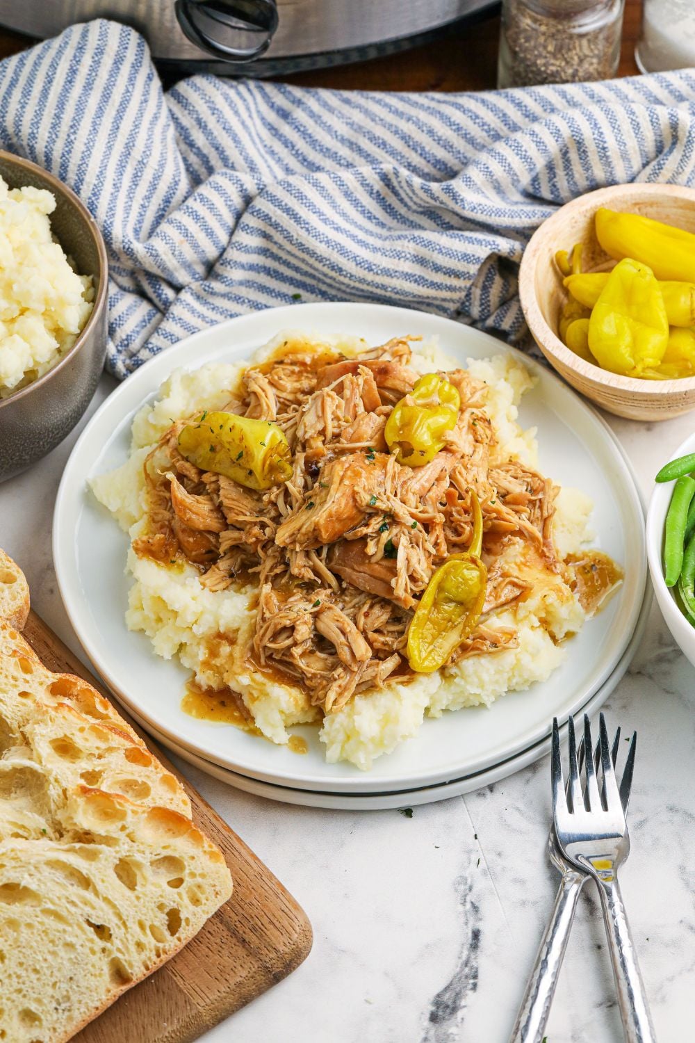 mashed potatoes and chicken on plate with peppers and bread around it on table