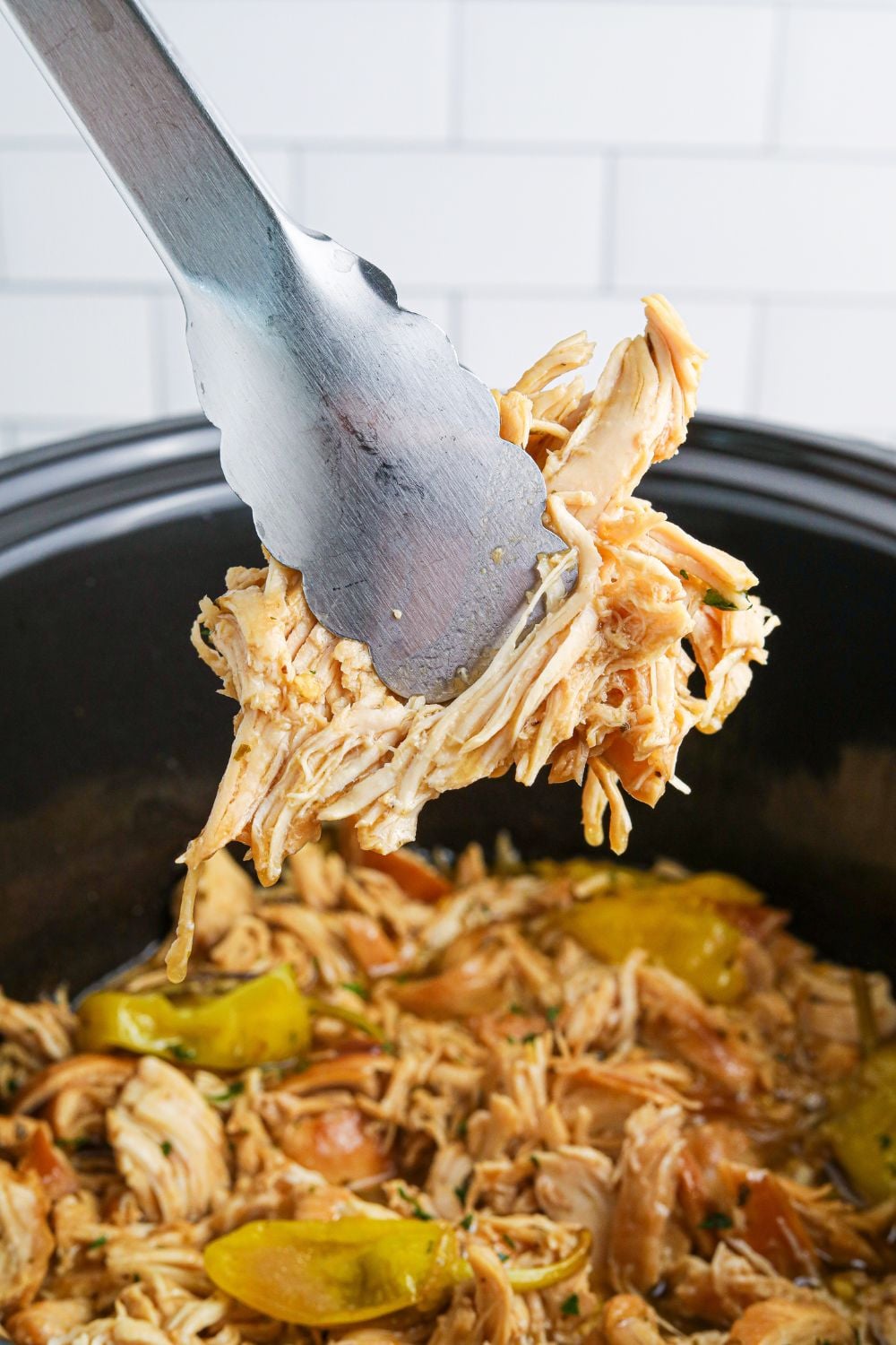 tongs with shredded chicken in it over the mississippi chicken in crockpot