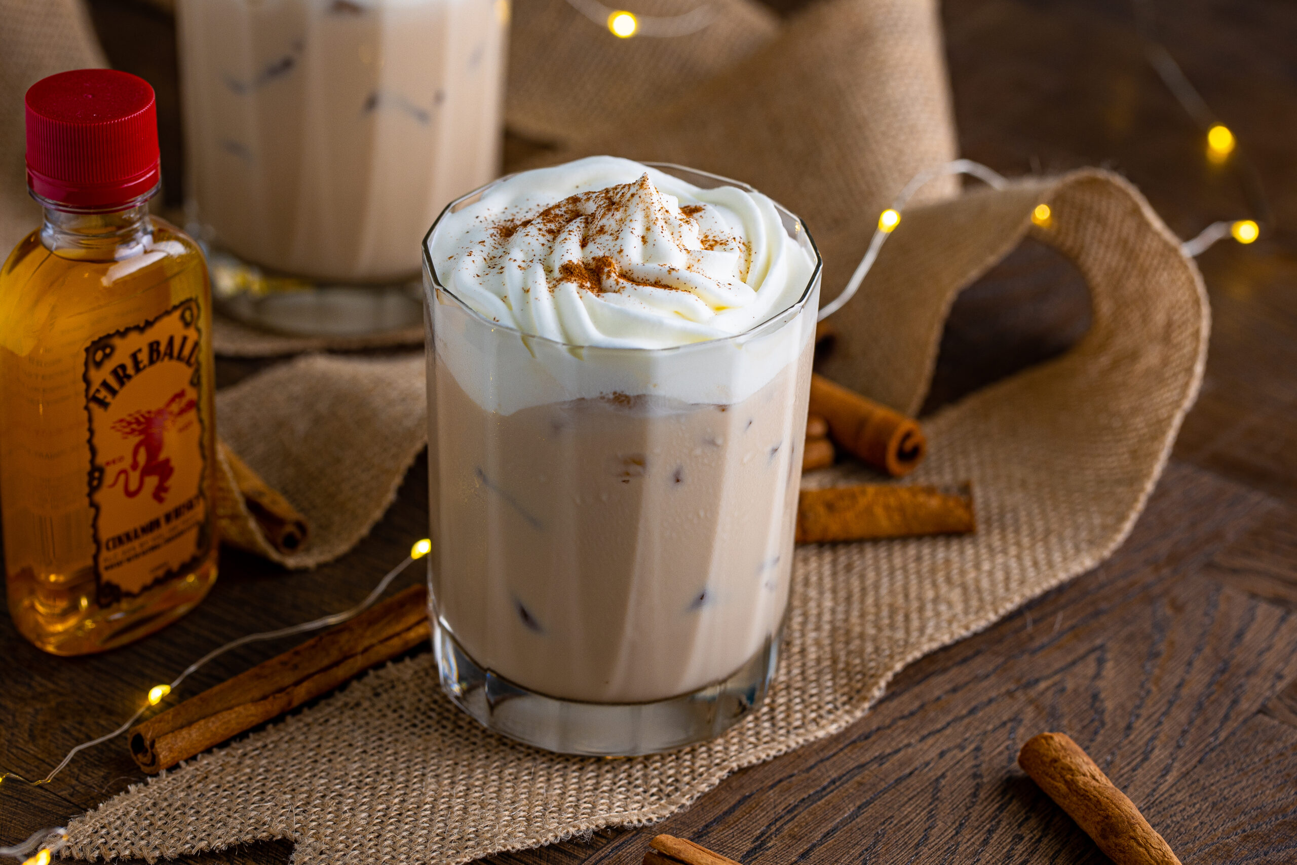 The cinnamon roll cocktail in a clear glass topped with whipped cream and dusted with cinnamon 