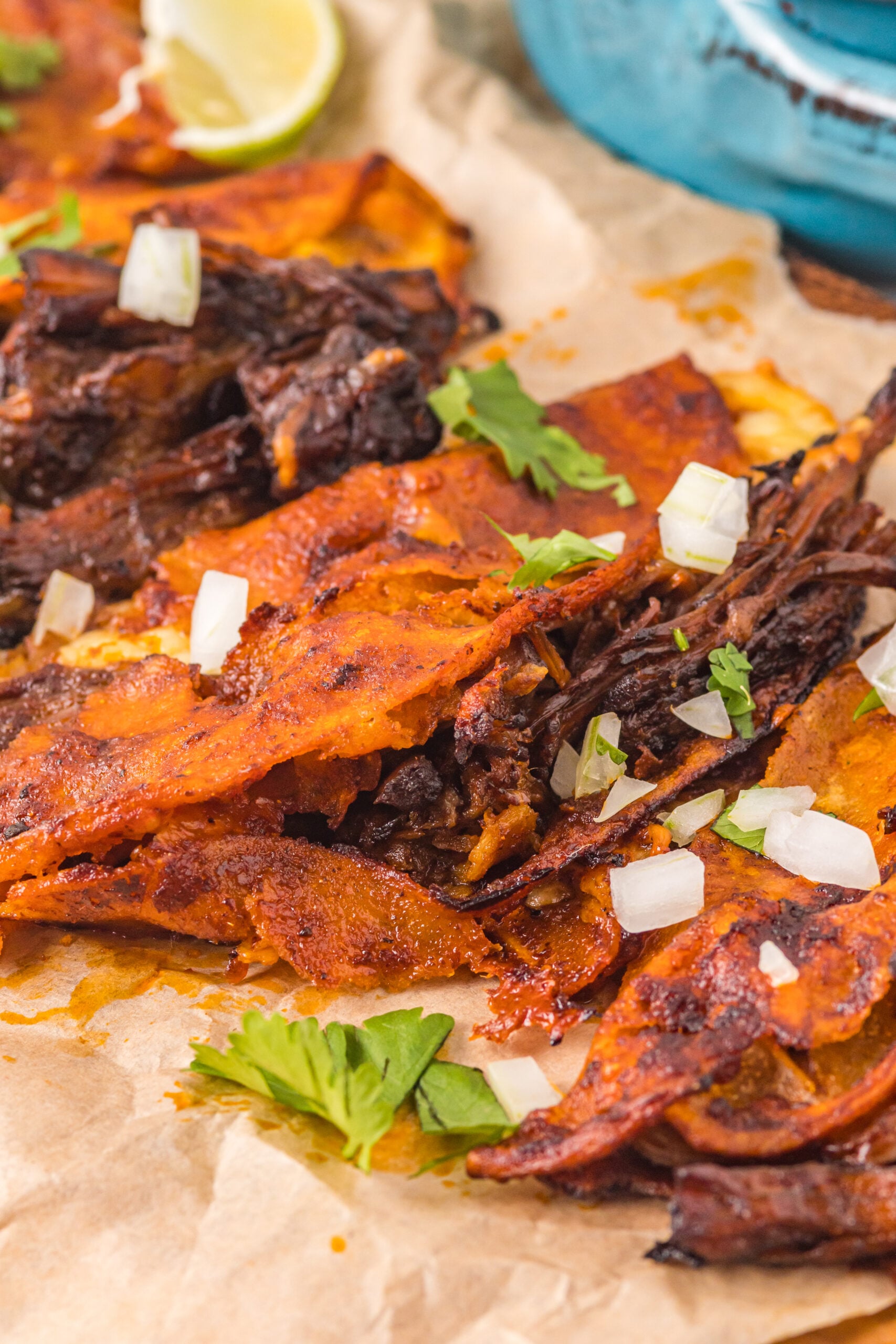 Close up view of Birria Tacos on a wooden board garnished with onion and cilantro.