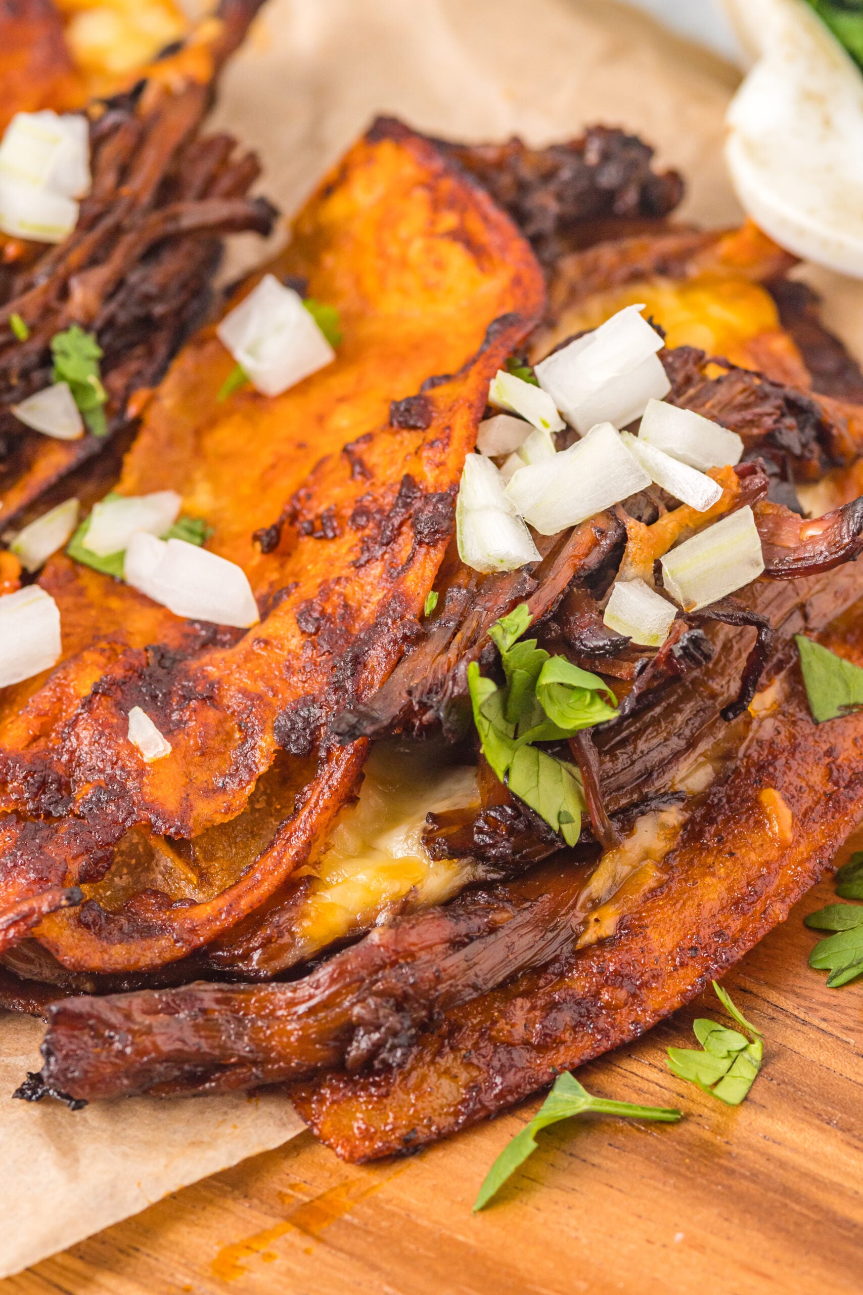 Overhead view of Birria Tacos on a wooden board garnished with onion and cilantro.