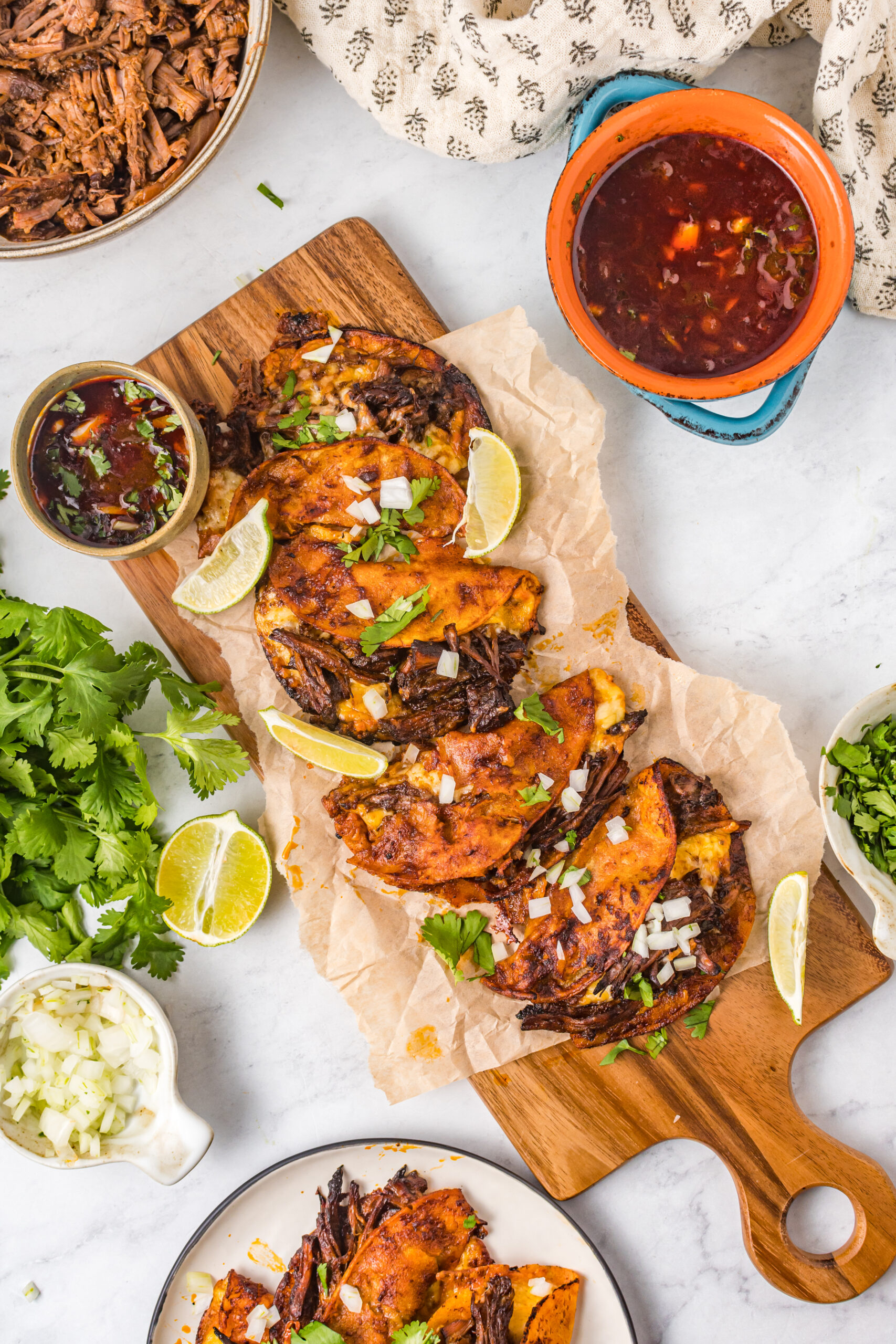 Overhead view of Birria Tacos on a wooden board garnished with onion and cilantro.
