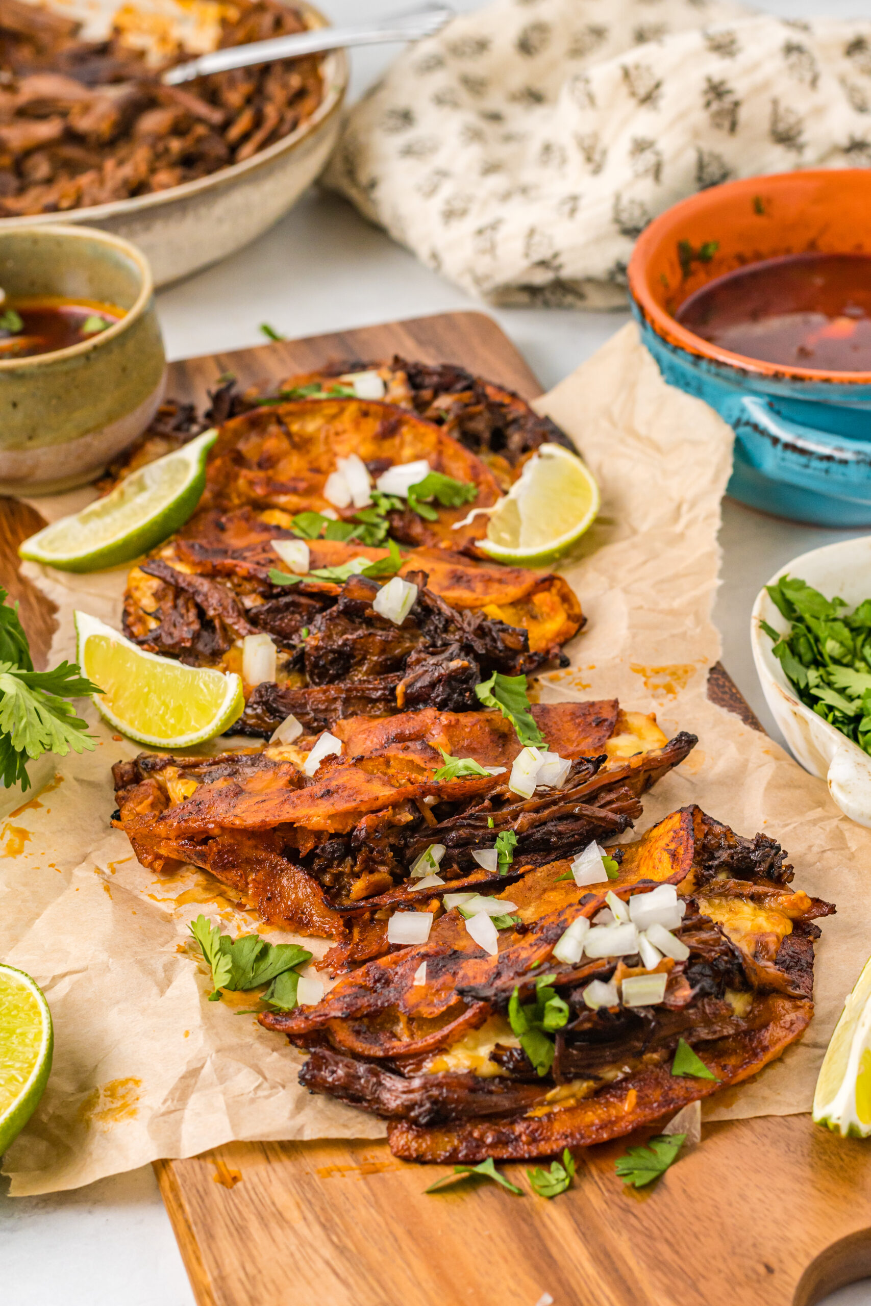 Front view of Birria Tacos on a wooden board garnished with onion and cilantro.