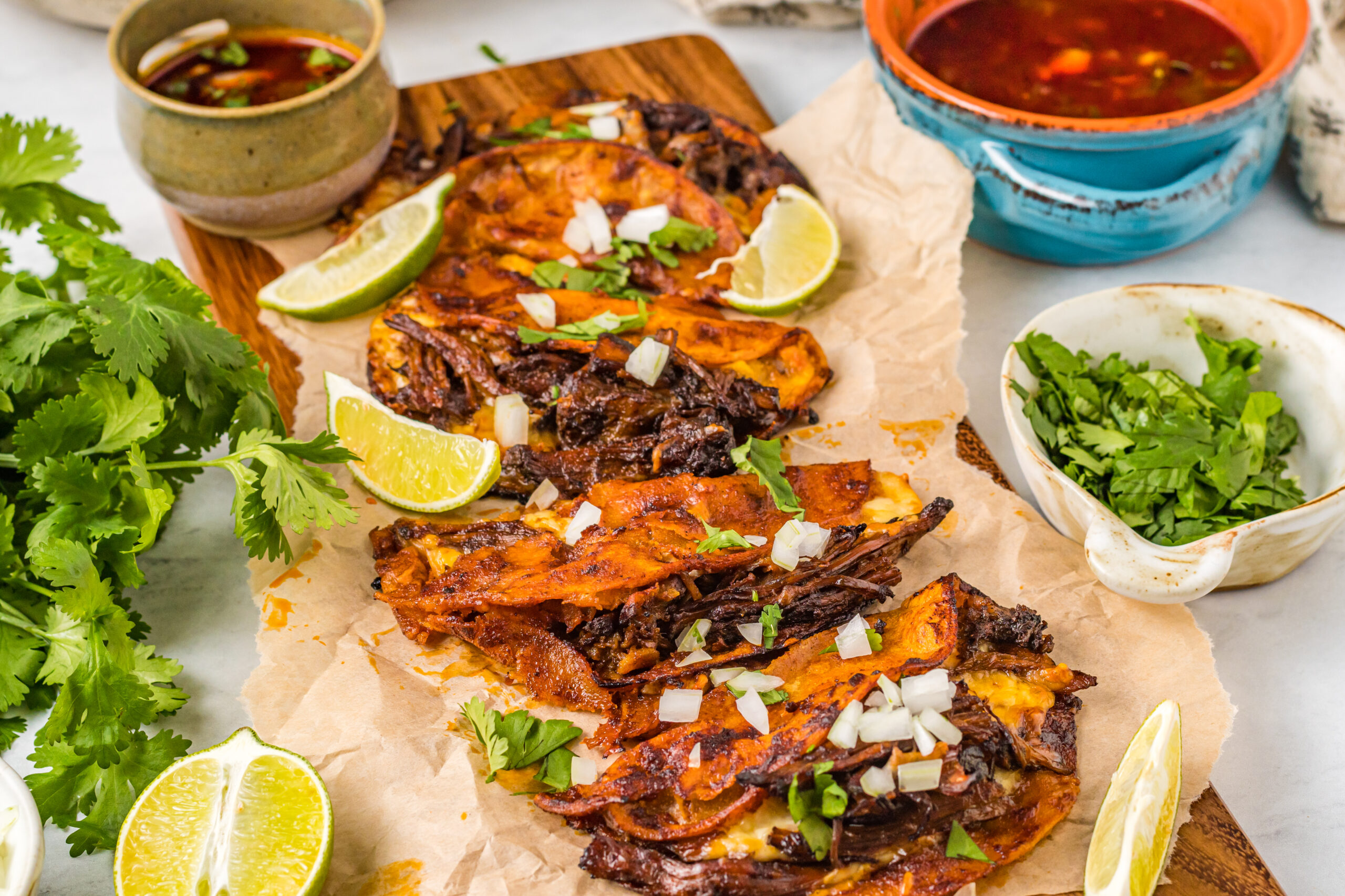 Front view of Birria Tacos on a wooden board garnished with onion and cilantro.