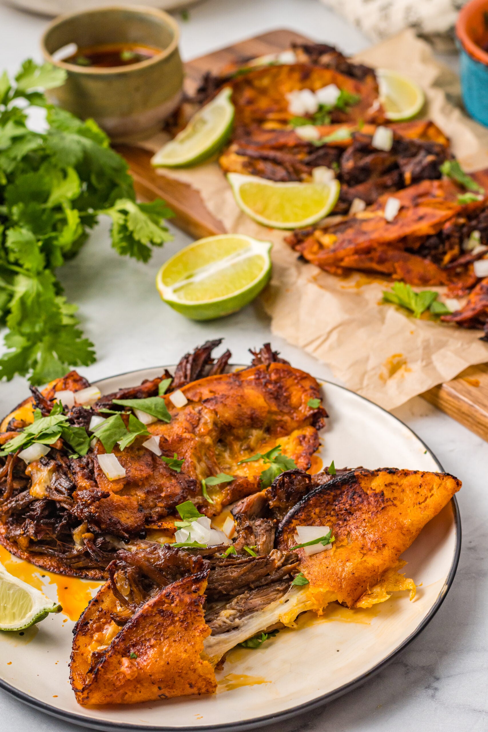 Front view of Birria Tacos on a white plate with one taco cut in half.