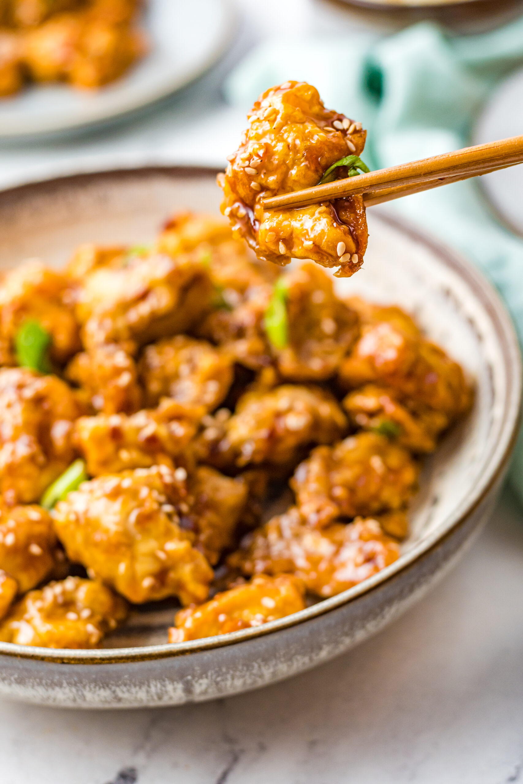 Close up view of chopsticks hold a piece of Air Fryer General Tsos Chicken.