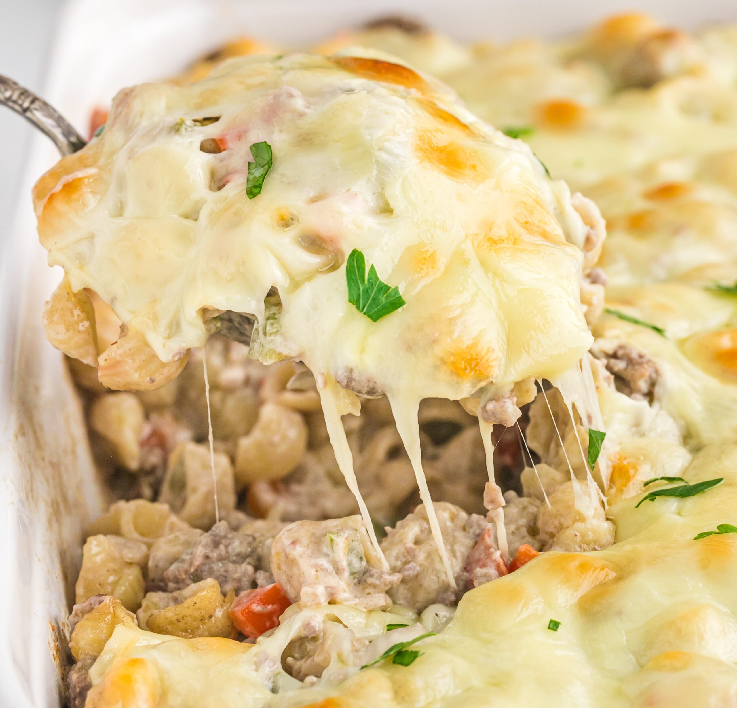Front view of Philly Cheesesteak Casserole in a white baking dish with a silver spoon removing a spoon full.
