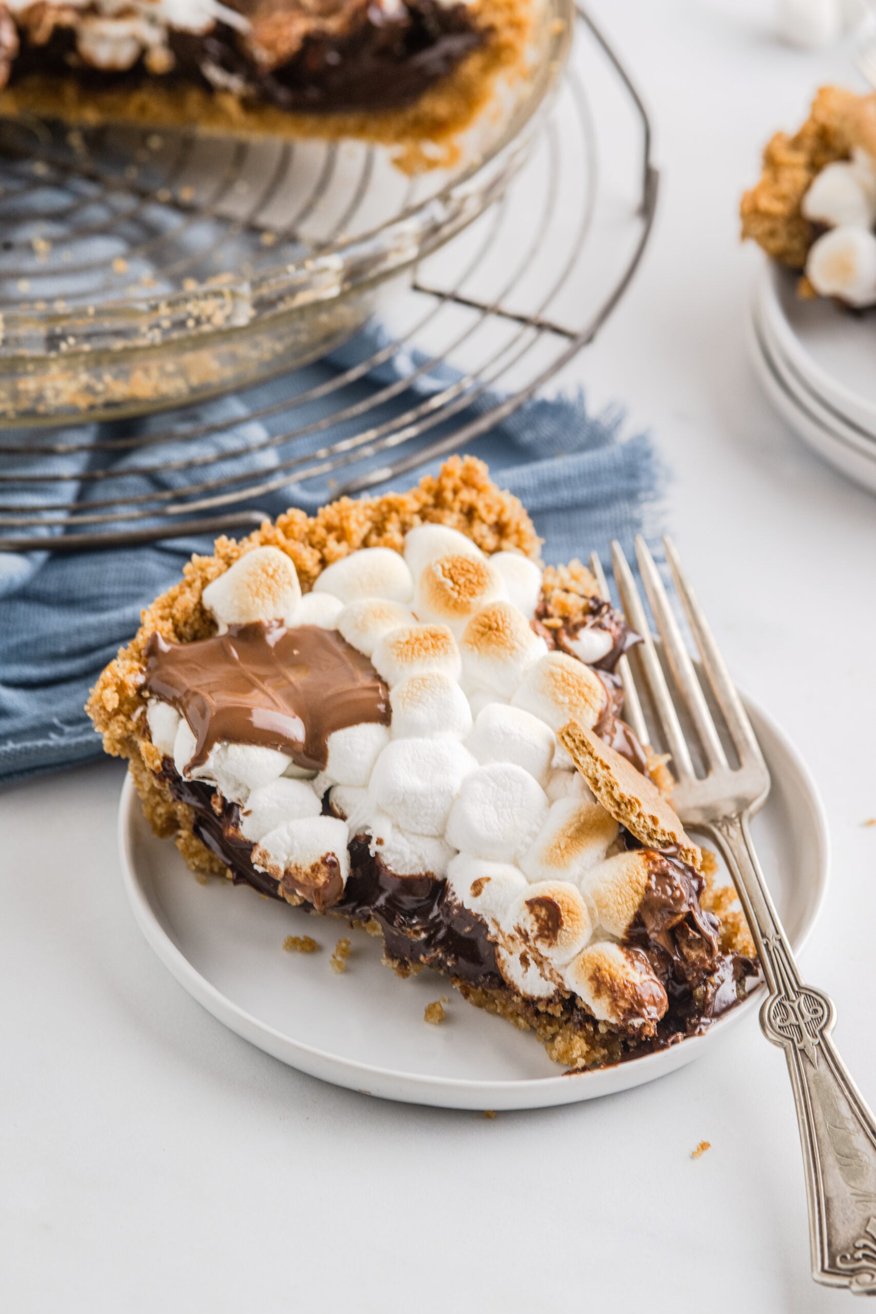 A piece of S'mores Pie on a white plate with a silver fork. 