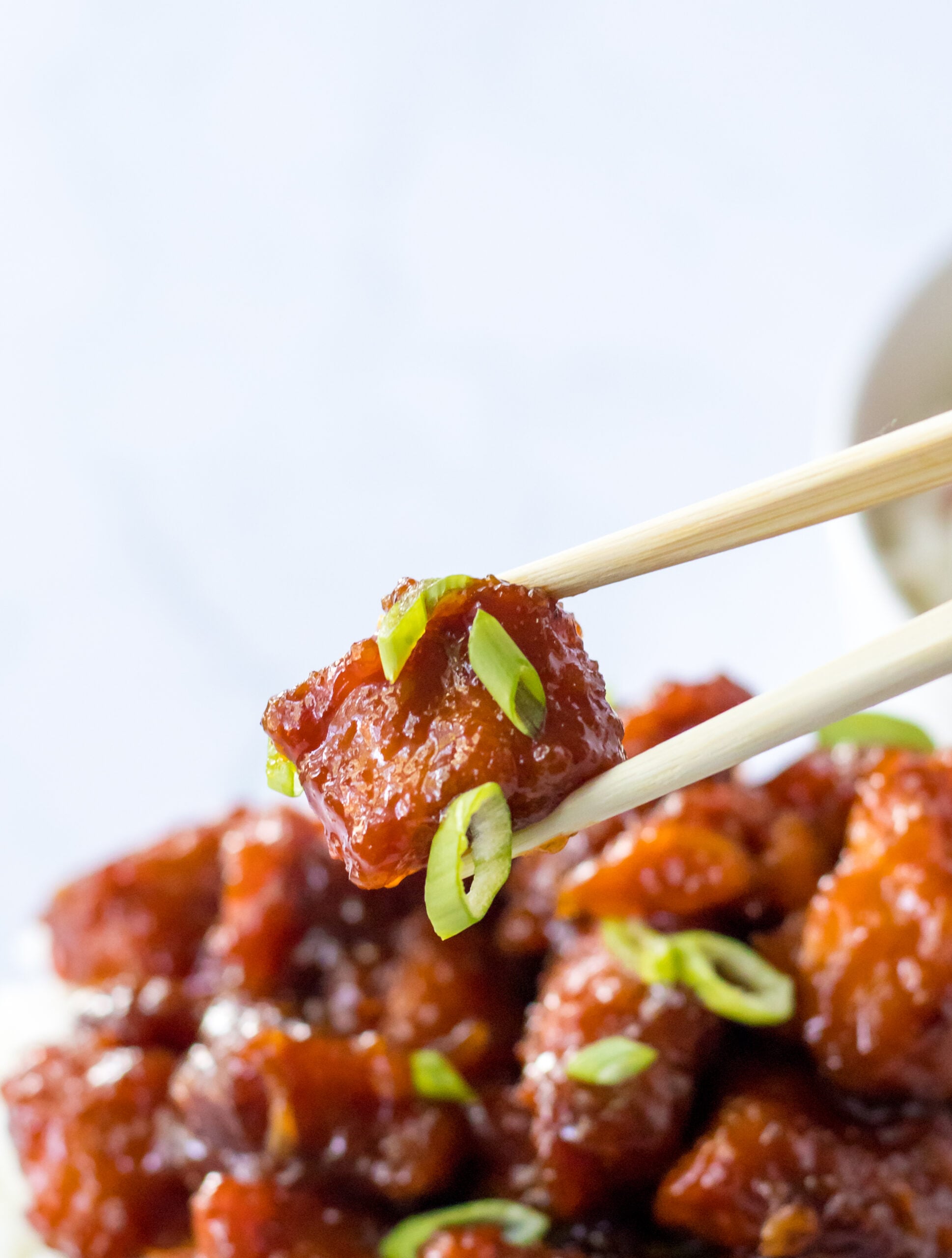 Close up view of chopsticks holding a piece of Slow Cooker Firecracker Chicken.