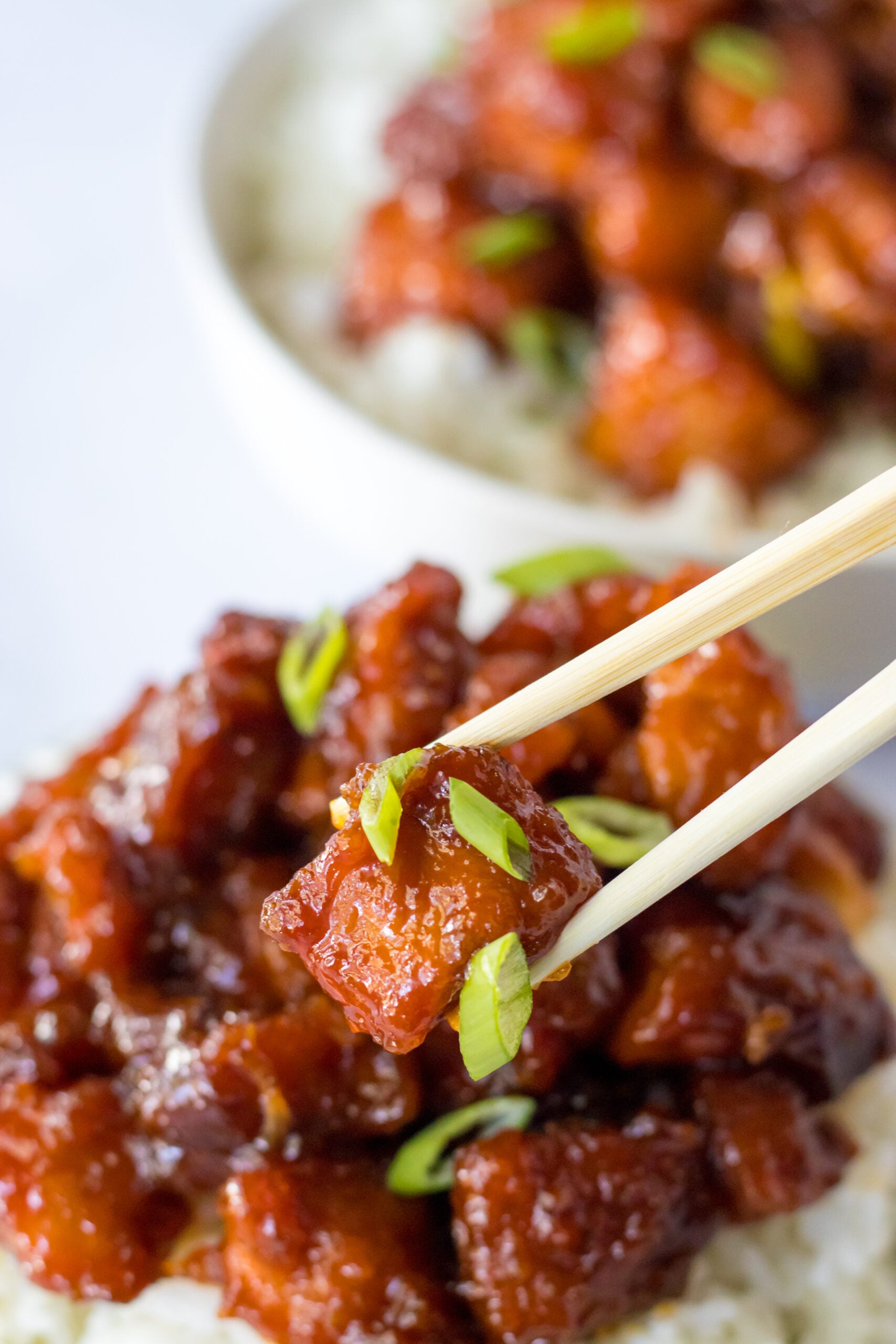 Close up view of chopsticks holding a piece of Slow Cooker Firecracker Chicken.