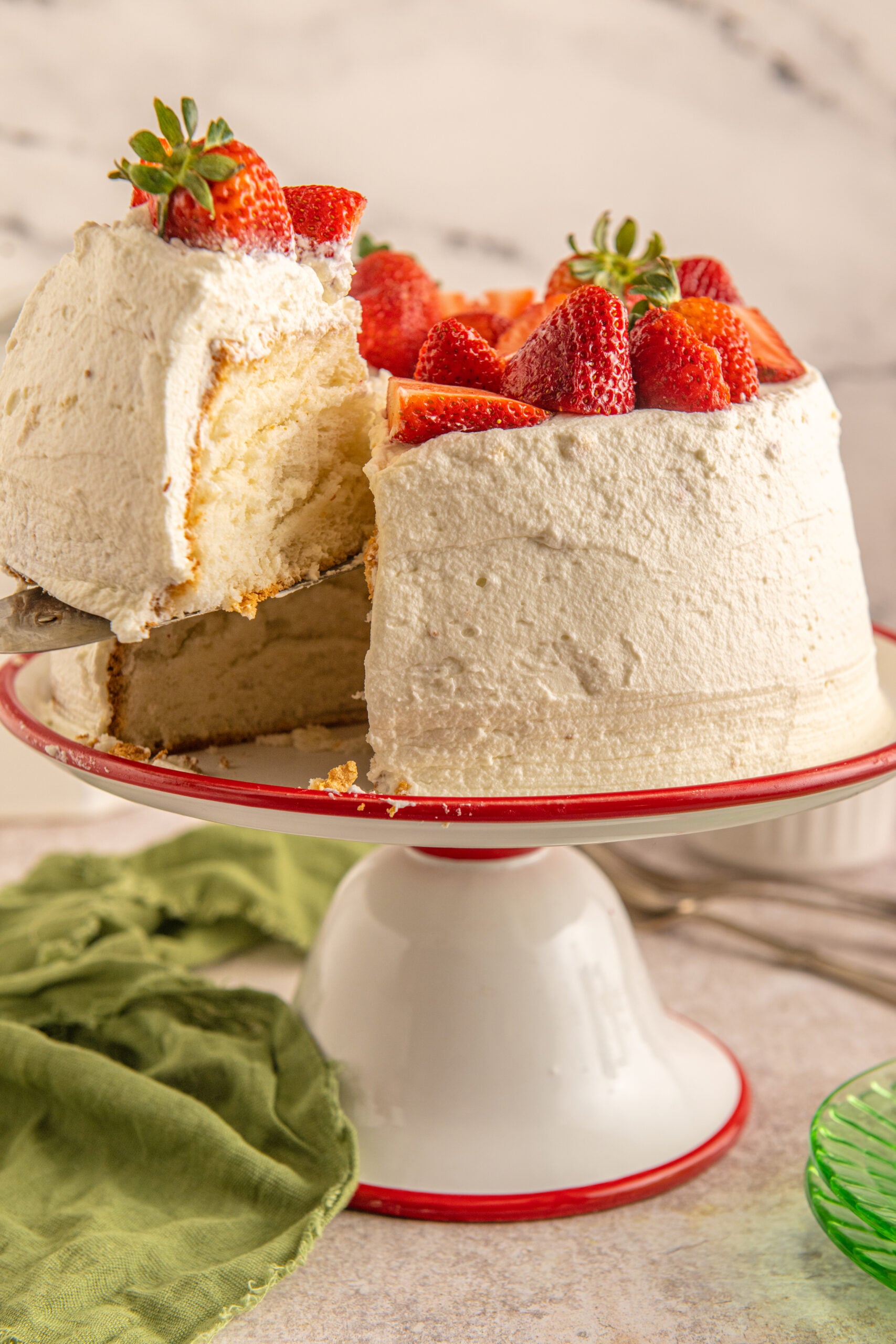 A piece of Strawberry Angel Food Cake being removed from a red and white cake stand with a silver spatula.