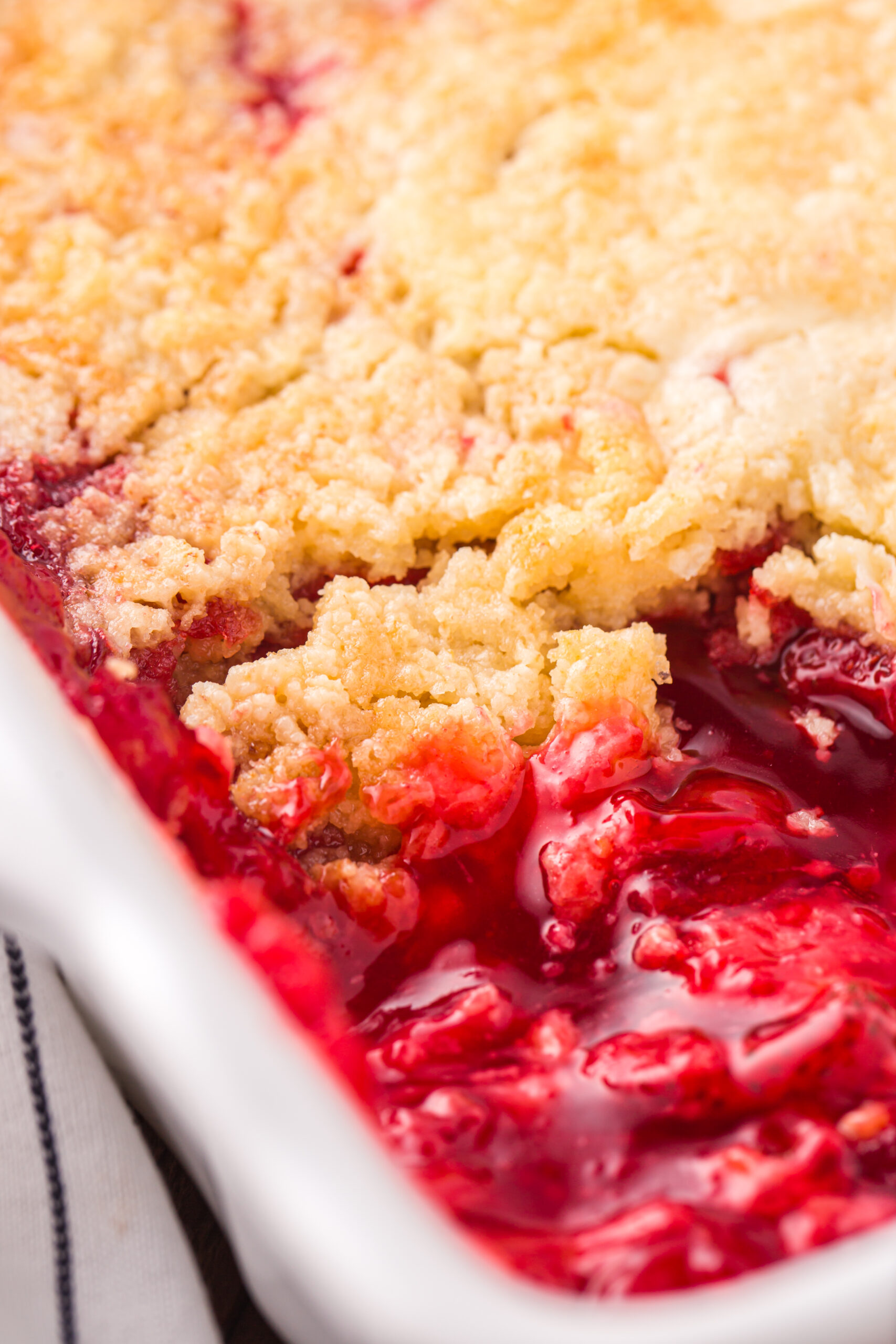 Close up view of Strawberry Dump Cake in a white baking dish with a serving removed.