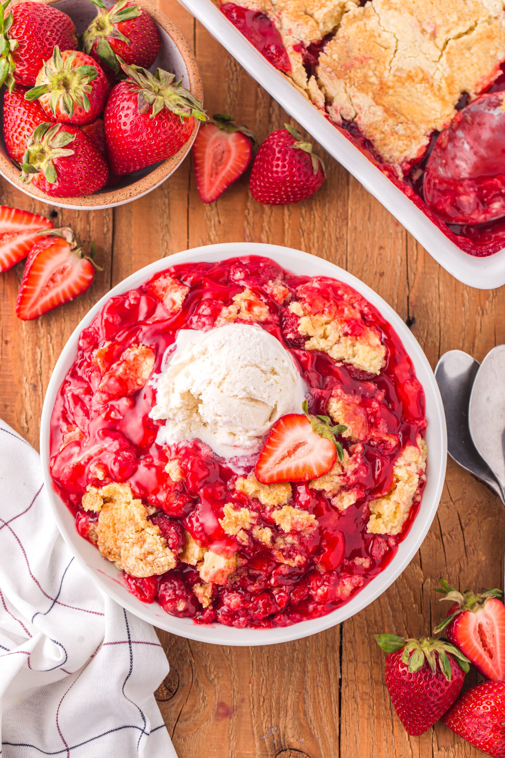 far away overhead view of a serving of Strawberry Dump Cake in a white bowl topped with a scoop of ice cream.