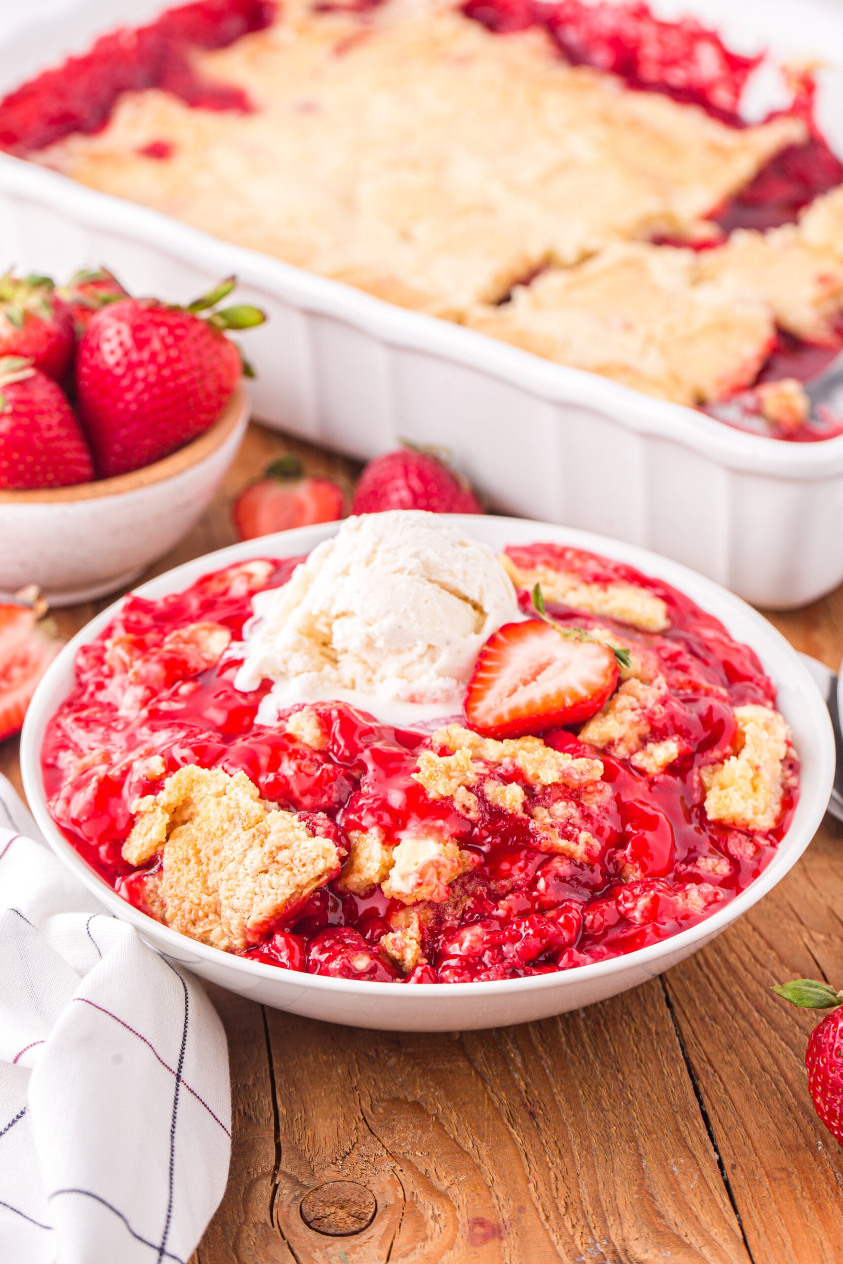 Front view of a serving of Strawberry Dump Cake in a white bowl topped with a scoop of ice cream.