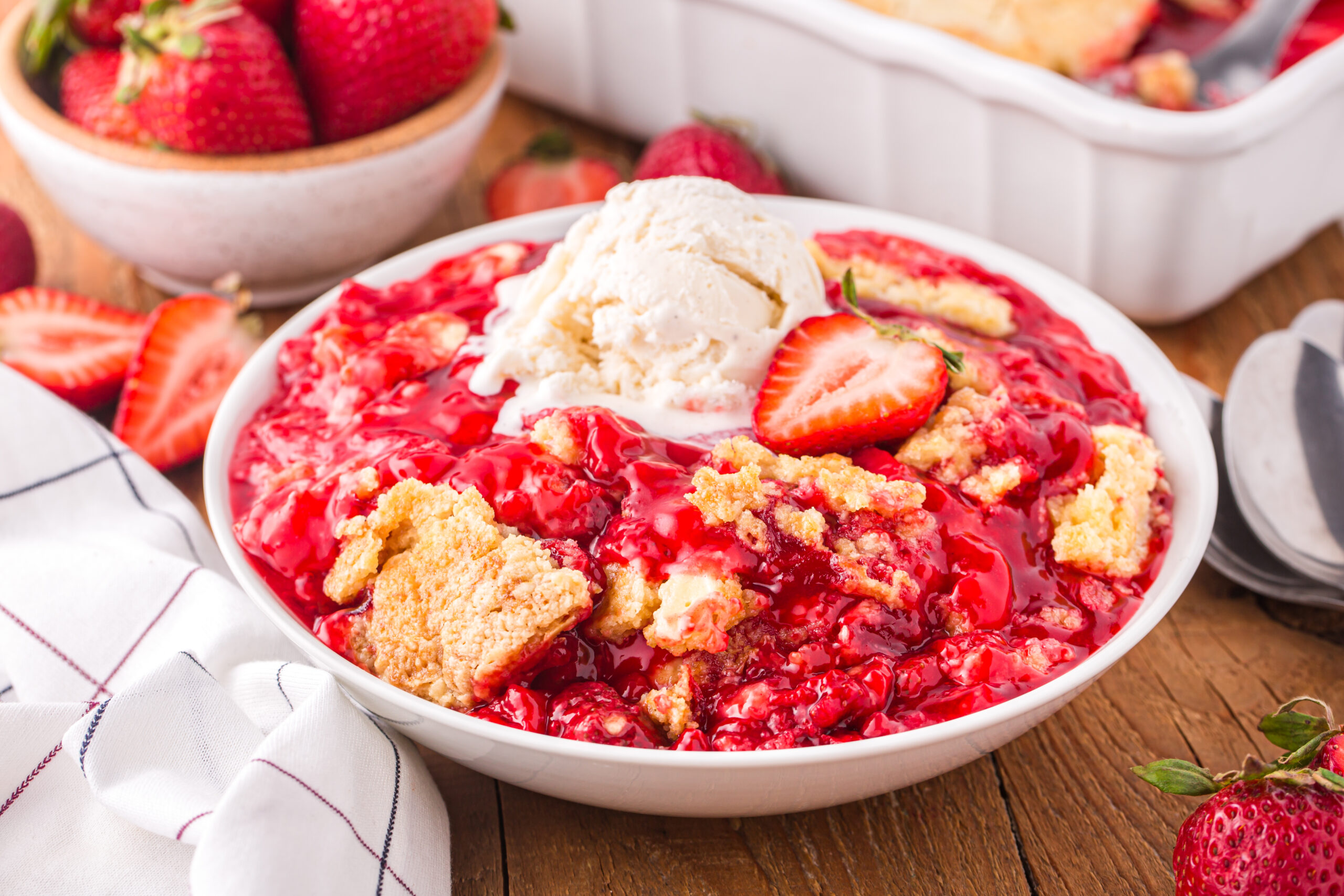 Front view of a serving of Strawberry Dump Cake in a white bowl topped with a scoop of ice cream.