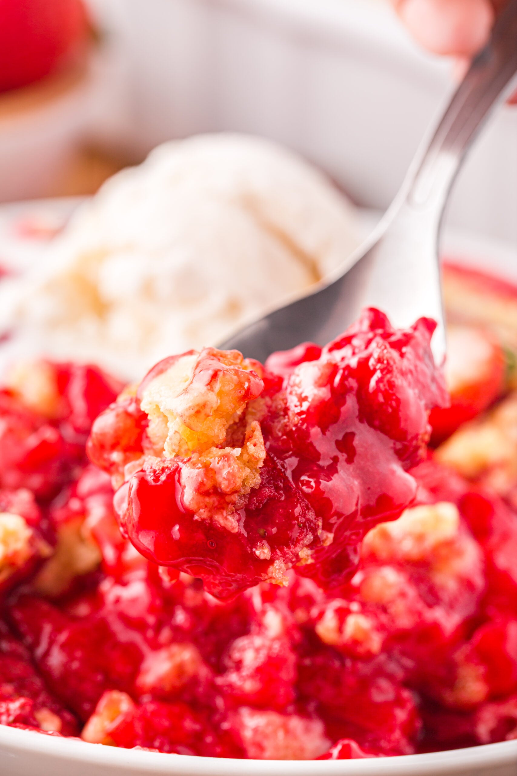 Close up view of a bite of Strawberry Dump Cake on a silver spoon.