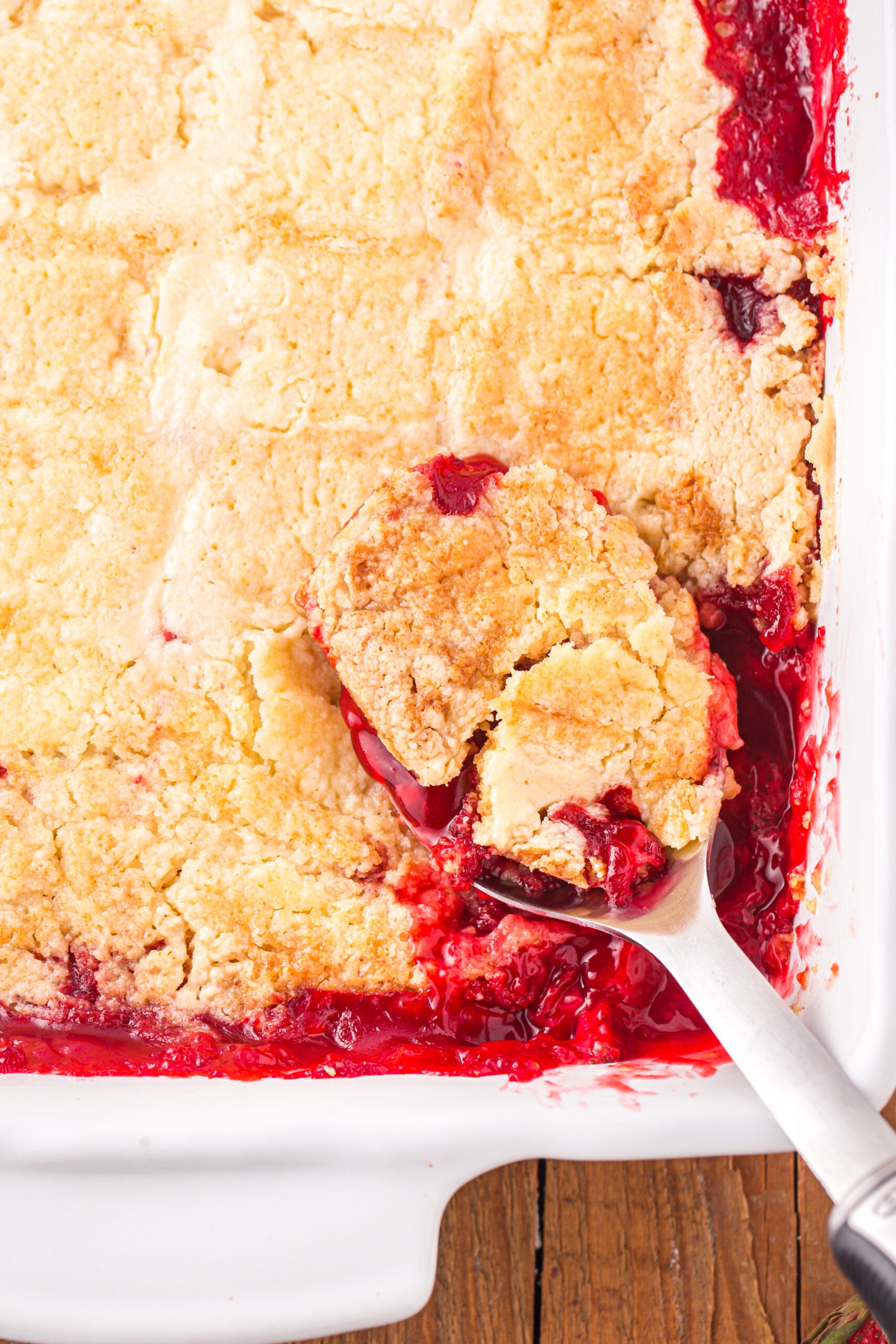 Close up view of a serving spoon removing a serving of Strawberry Dump Cake.
