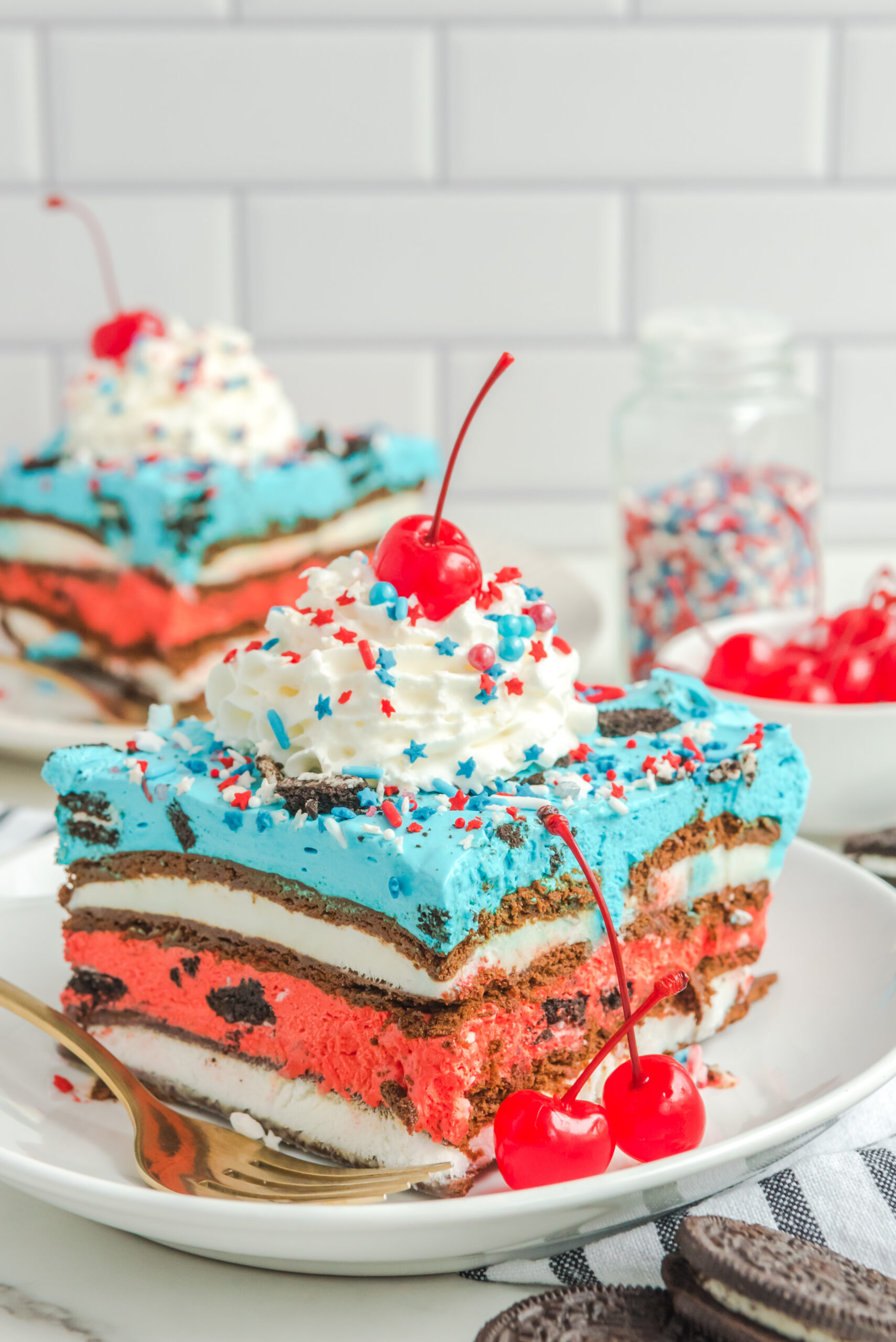Front view of a slice of Patriotic Ice Cream Sandwich Cake topped with whipped cream and cherry on a white plate.