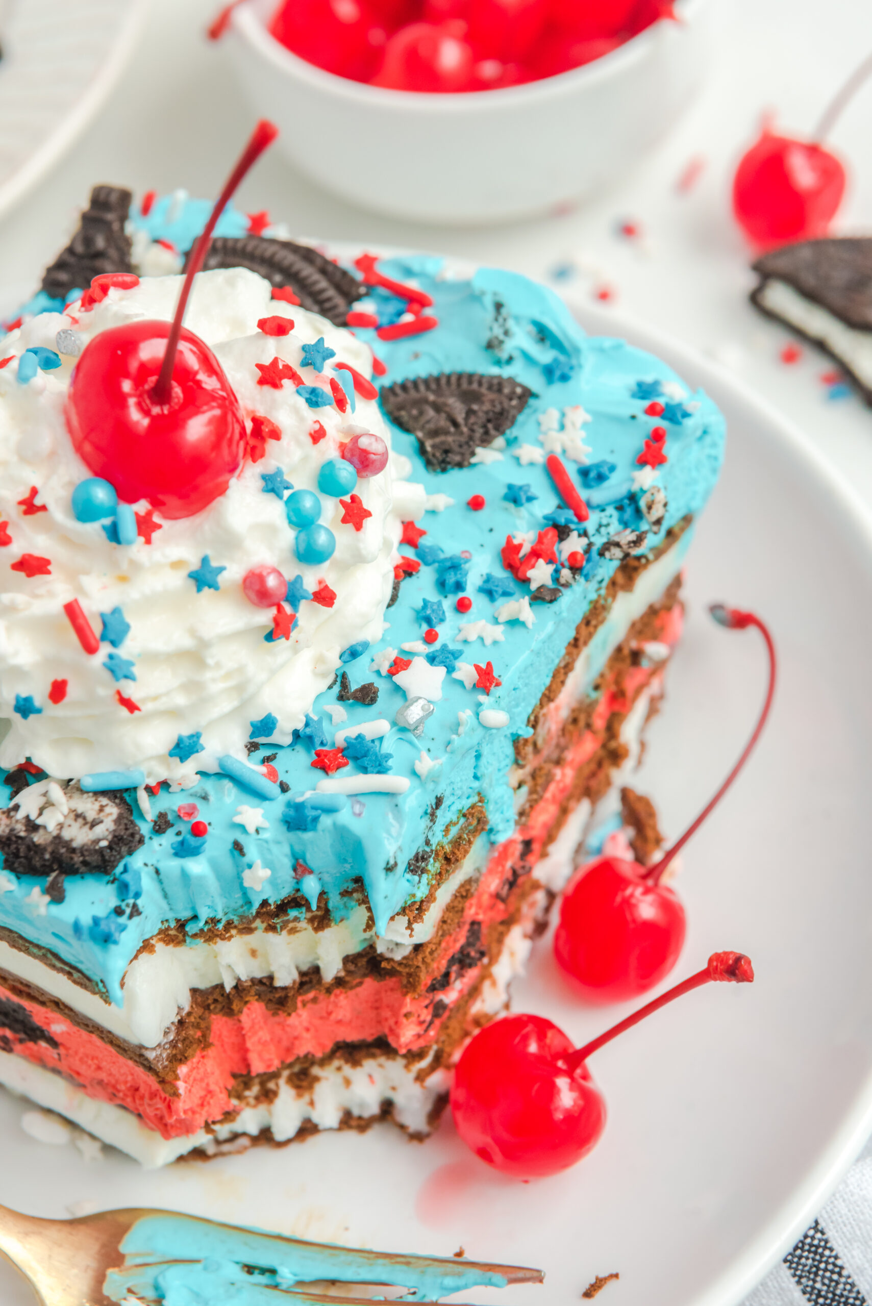 Close up view of a slice of Patriotic Ice Cream Sandwich Cake topped with whipped cream and cherry.