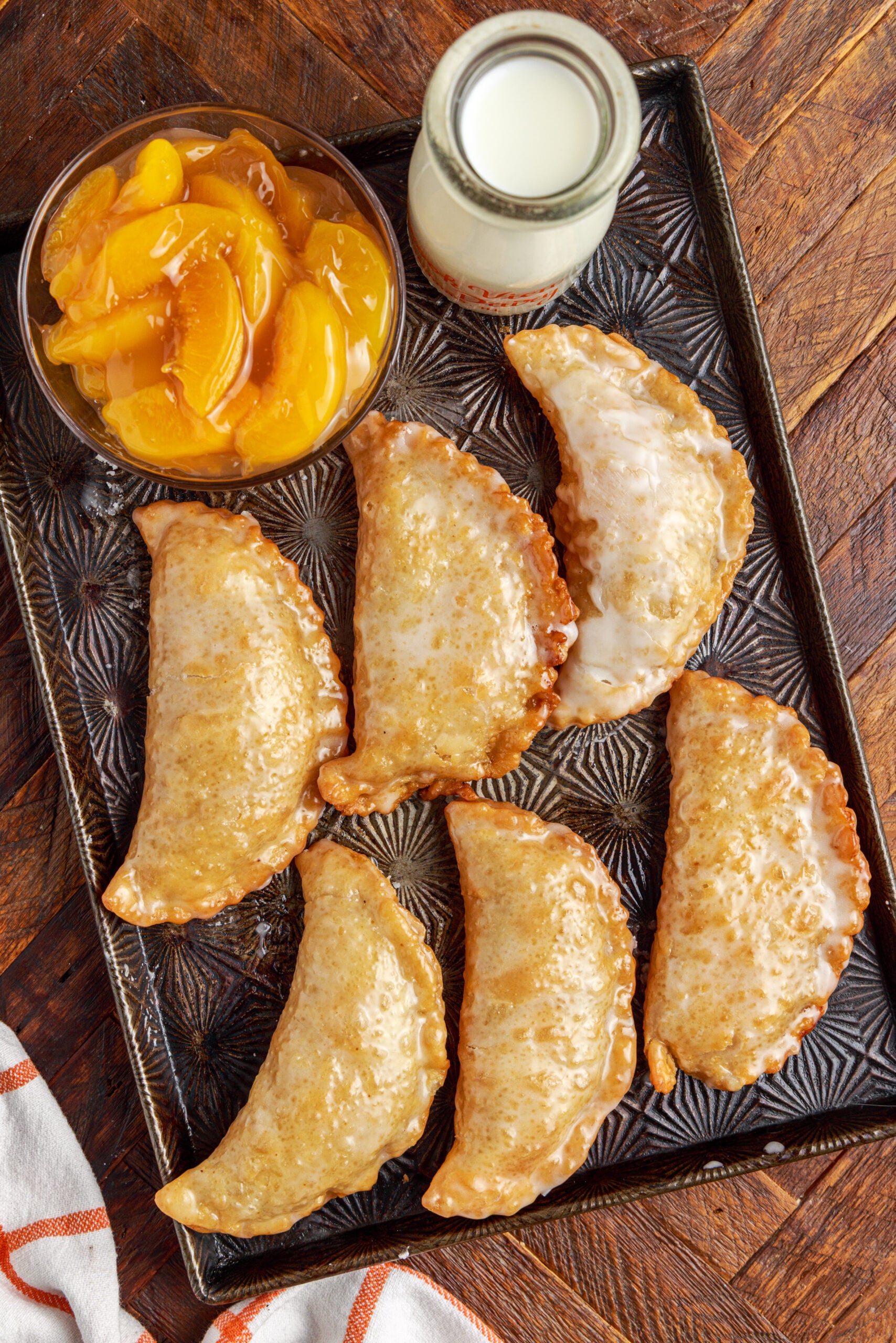 peach hand pies on a silver serving tray with milk and a bowl of peaches