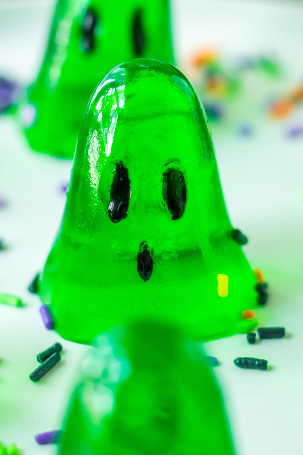 close up of a green ghost jello shot on plate with Halloween sprinkles around it