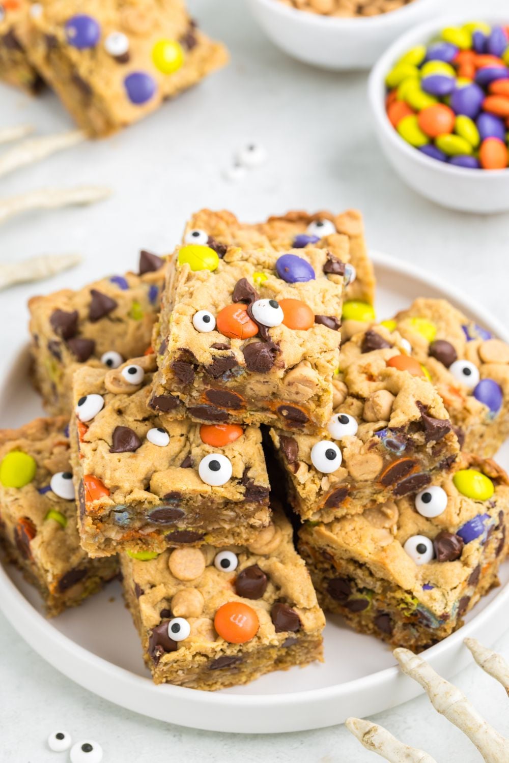 a stack of many halloween monster cookie bars on a white plate