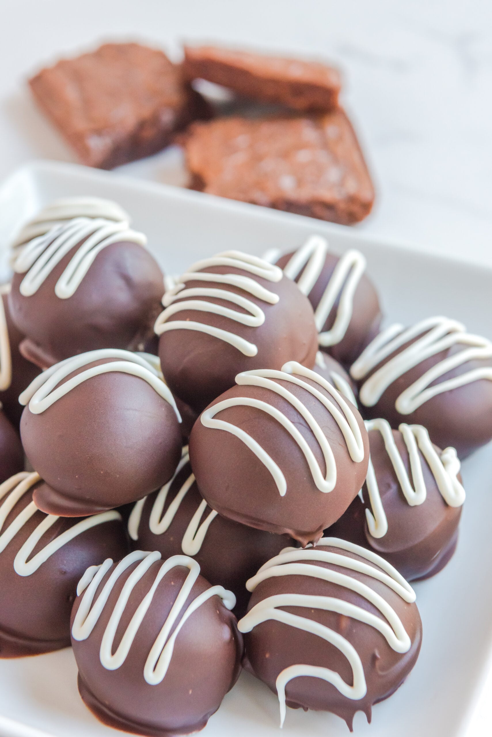 Brownie Bite Truffles on a white plate with brownies stacked behind them
