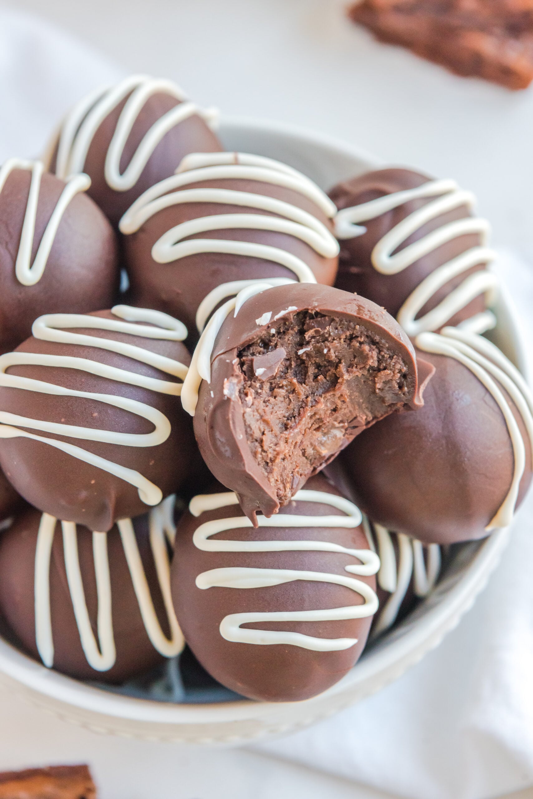 Brownie Bite Truffles drizzled with white chocolate and in a white bowl with a bite taken out of the top one
